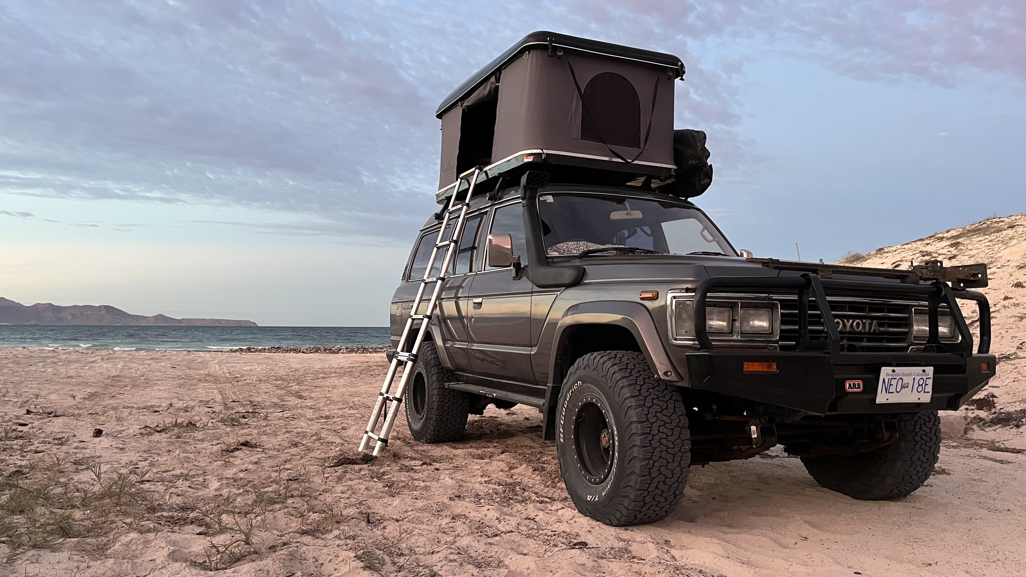 Overland-ready Toyota Land Cruiser with rooftop tent on a beach, ideal for an RV rental alternative for off-grid camping adventures.. Toyota LandCruiser HJ61 VX 1989