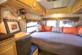 Step inside this cozy RV rental! A spacious bedroom features a large bed with pillows, multiple windows, and light wood overhead cabinets.. Pleasure Way Excel 2006