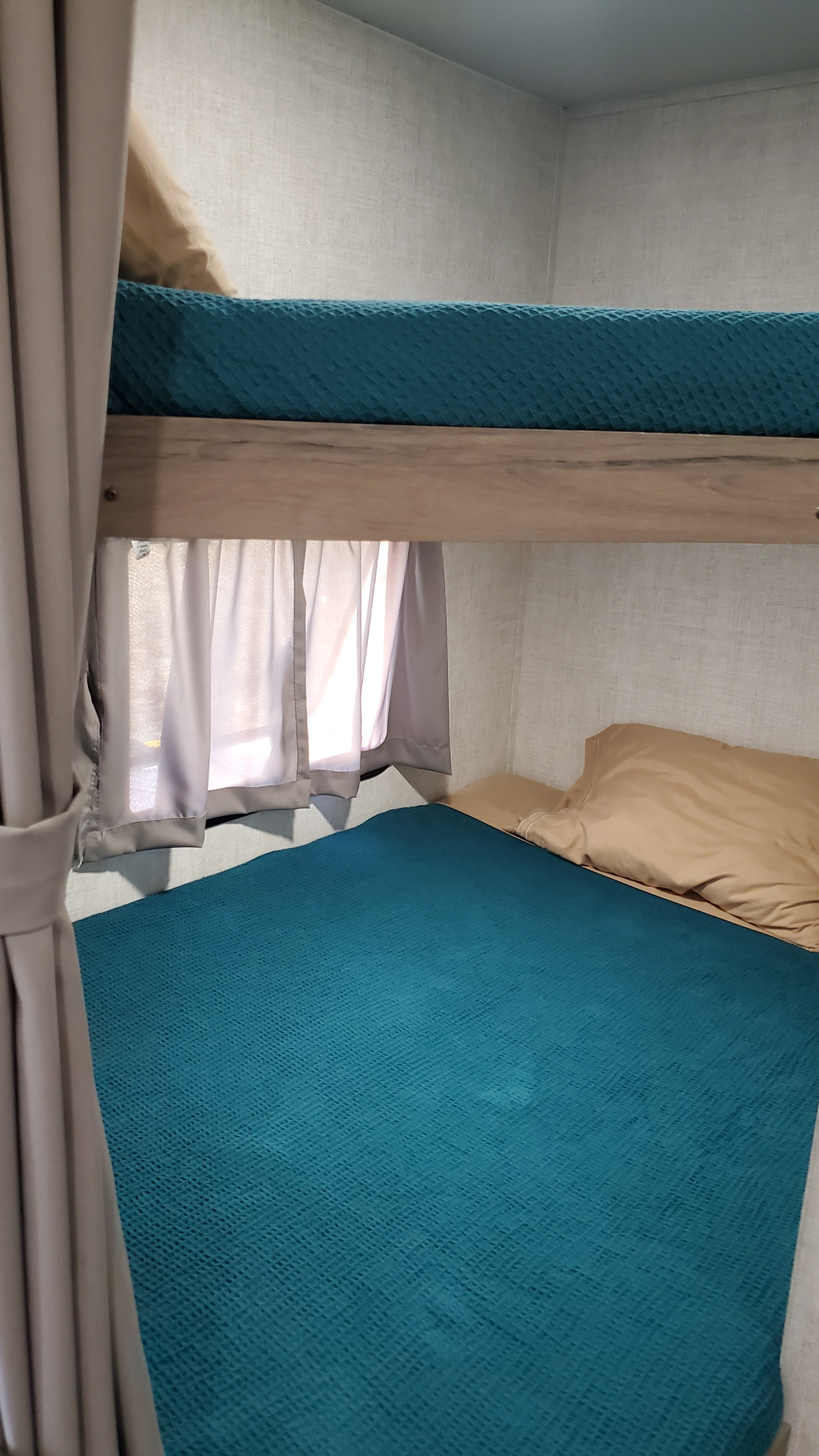 Cozy bunk beds in an RV rental, featuring teal bedspreads, tan pillows, and privacy curtains. Perfect for family adventures.. Gulf Stream Enlighten 2021