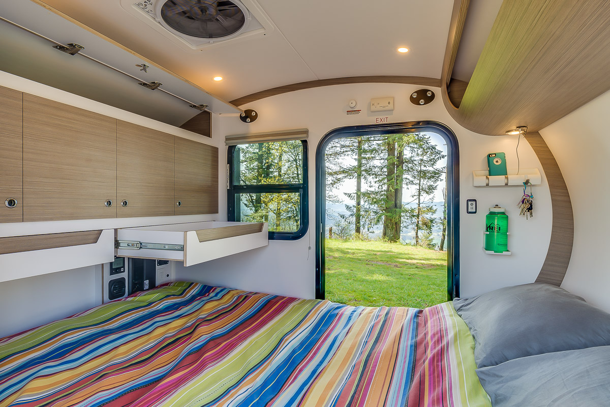 Modern RV rental interior with a colorful bed, smart storage, and a scenic view of nature through the open door and window.. Bean Trailer Bean Stock 2022