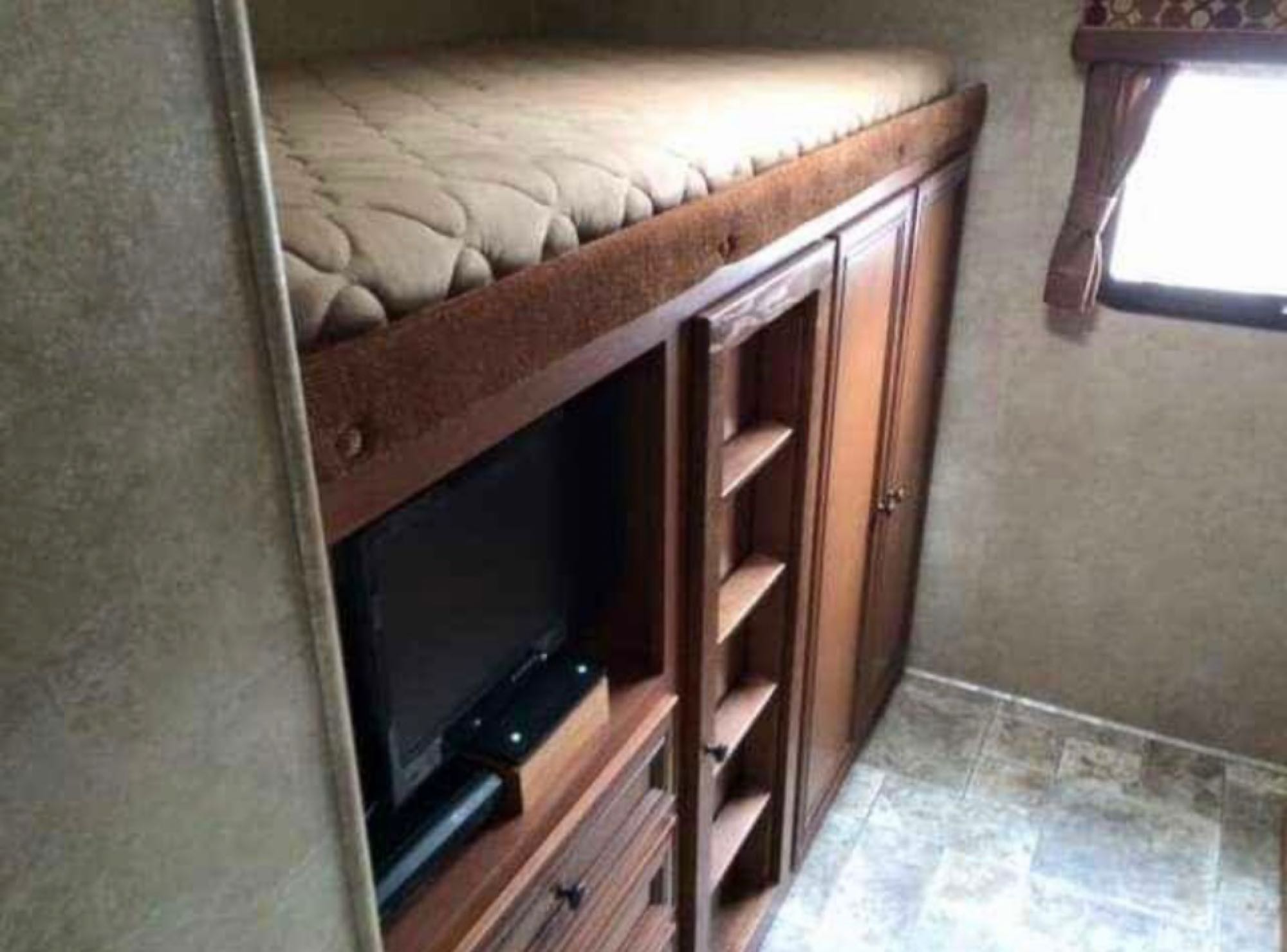 Inside an RV rental: a built-in bunk bed sits above a TV entertainment center and ample storage cabinets. A window is on the right.. Spree Spree Trailer 2014