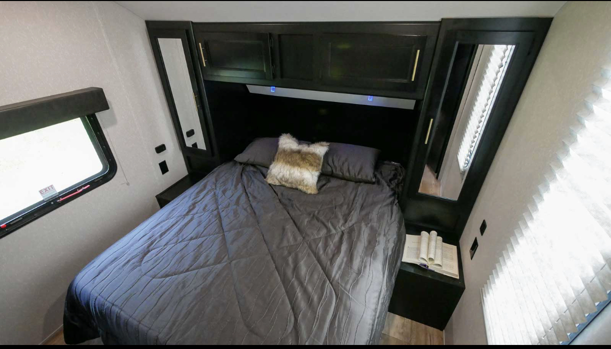 Functional RV rental bedroom features dark bedding, built-in storage, and windows, ideal for compact living.. Forest River Cherokee 2022