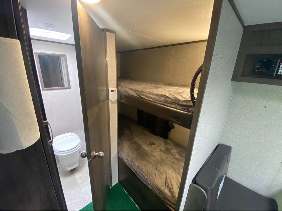 This RV rental interior shows a compact bathroom with a toilet, adjacent to cozy bunk beds, ideal for family travel.. Jayco Jay Flight SLX Baja Edition 2020