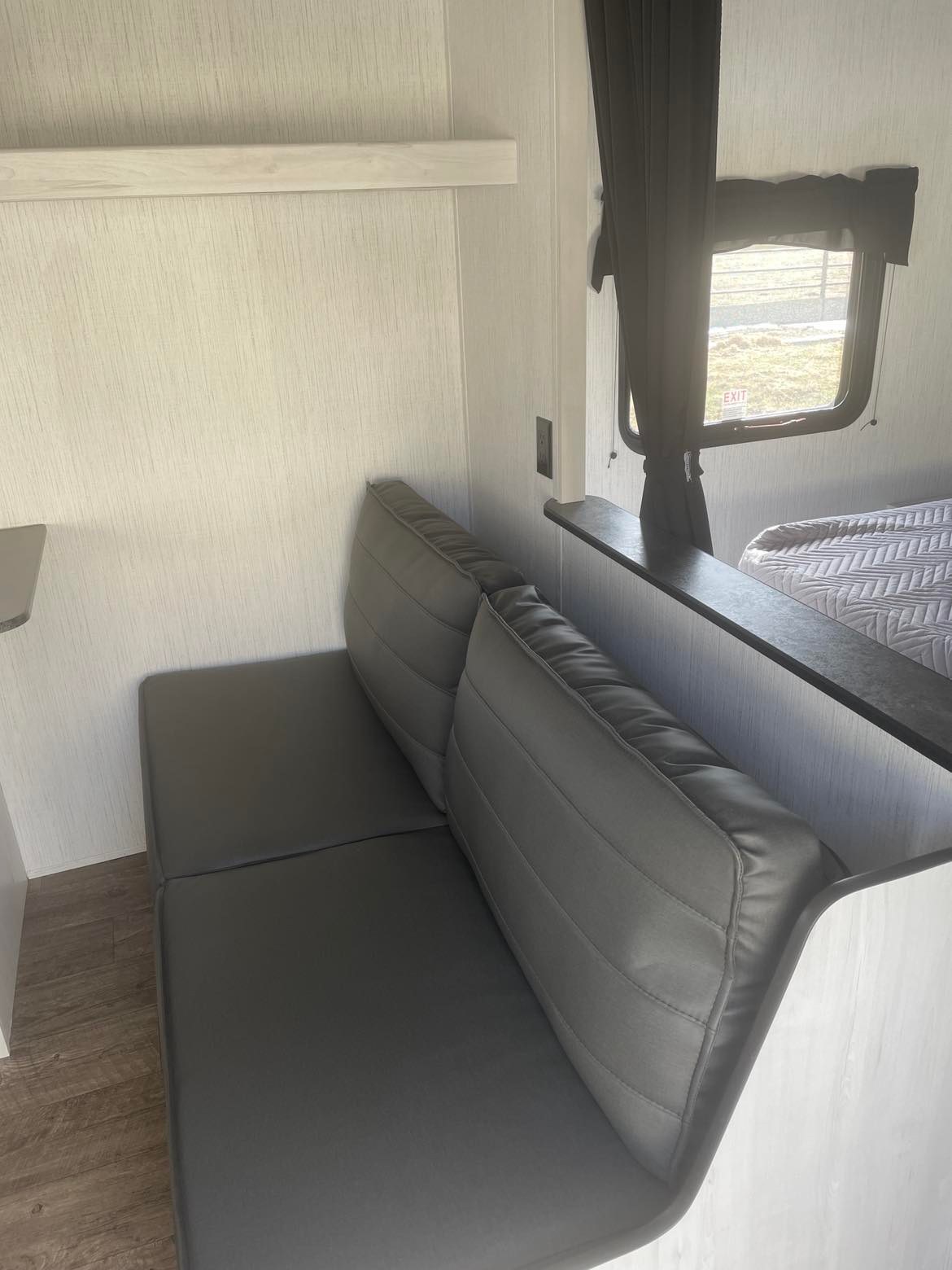 This RV rental offers a compact interior with modern grey dinette seating, a window, and a glimpse of the sleeping area.. Heartland RVs Trail Runner 2022