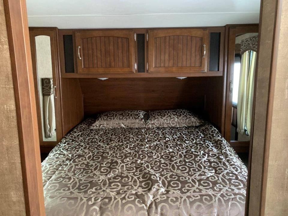 Cozy RV rental bedroom with patterned bedding, wooden cabinets, and mirrored storage on both sides of the bed.. Jayco White Hawk 2017