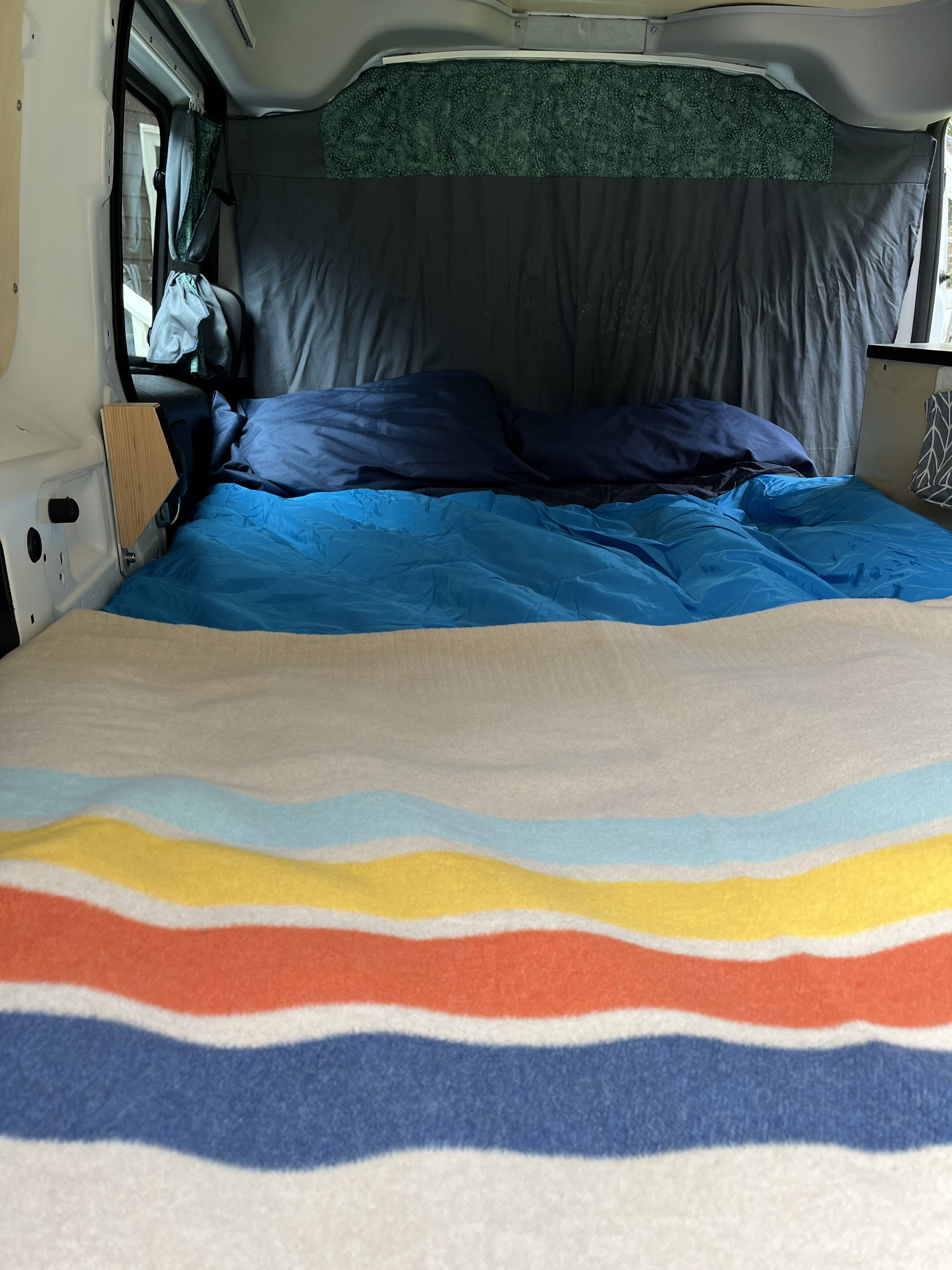Cozy RV rental sleeping area featuring a bright blue sleeping bag, navy pillows, and a vibrant striped blanket.. Dodge Ram 1500 2021