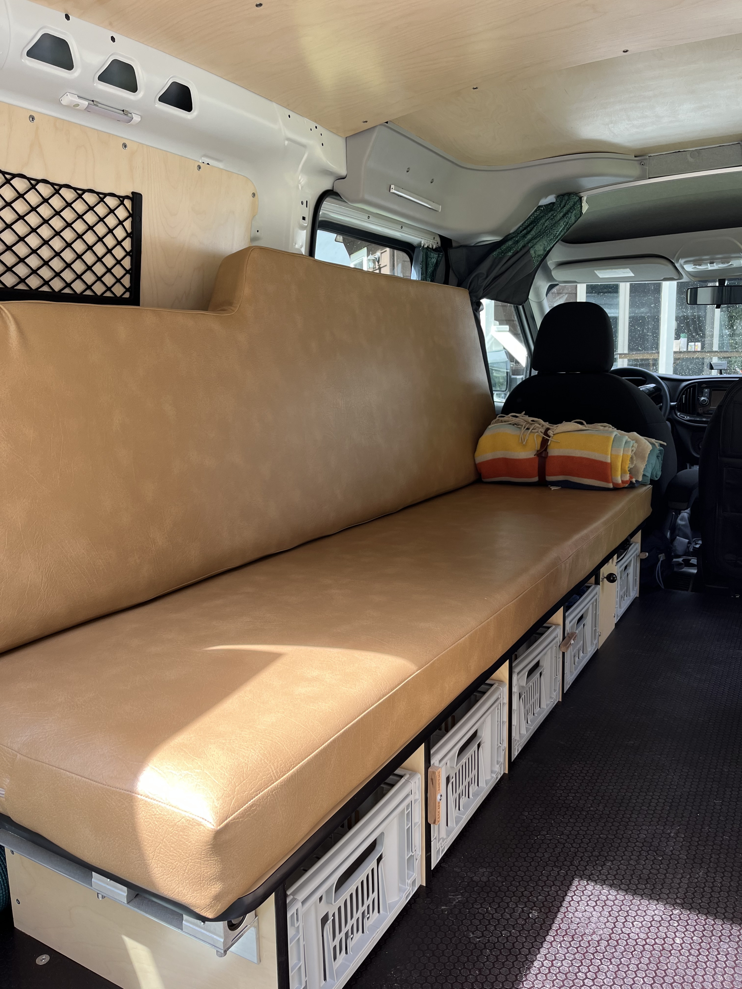 Spacious rv rental interior showing a custom tan bench seat with crate storage, wood paneling, and a cozy blanket.. Dodge Ram 1500 2021
