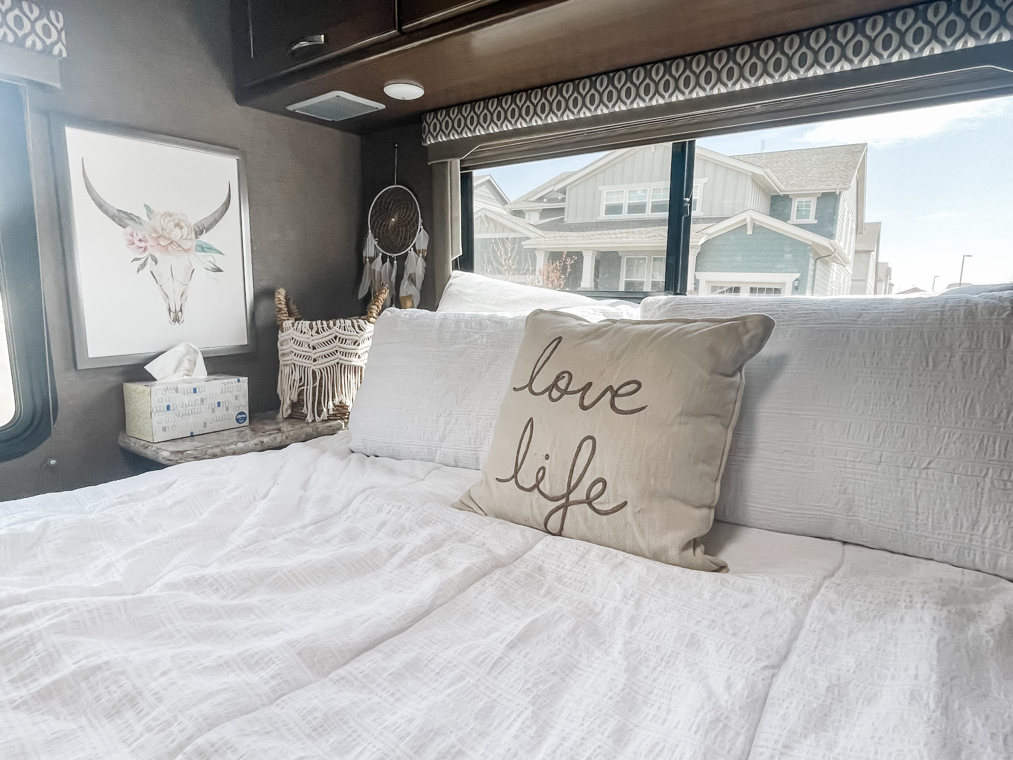 Cozy RV rental bedroom with white bedding, a 'love life' pillow, and a view of houses outside.. Thor Freedom Elite 2017