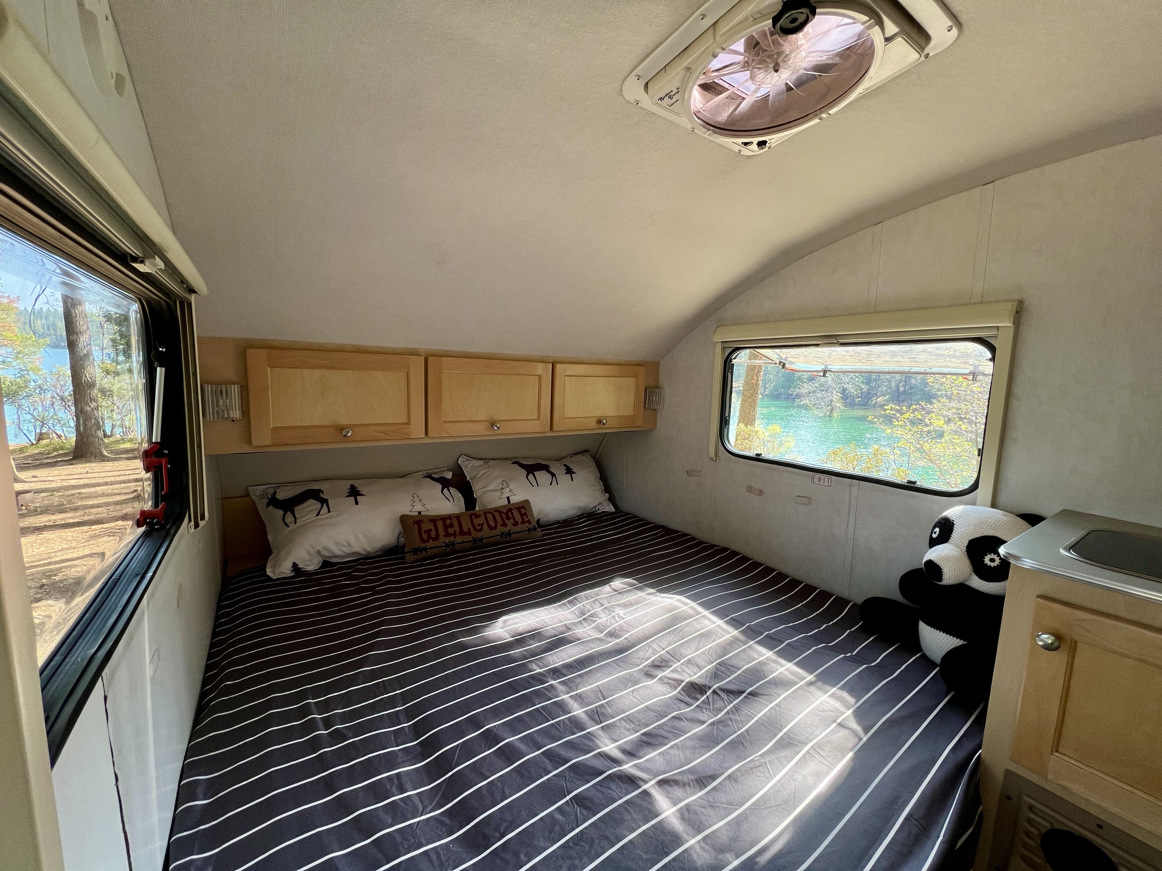 Cozy RV rental bedroom with striped bed, overhead storage, stunning lake views, and a friendly panda companion.. TAB T1 2007
