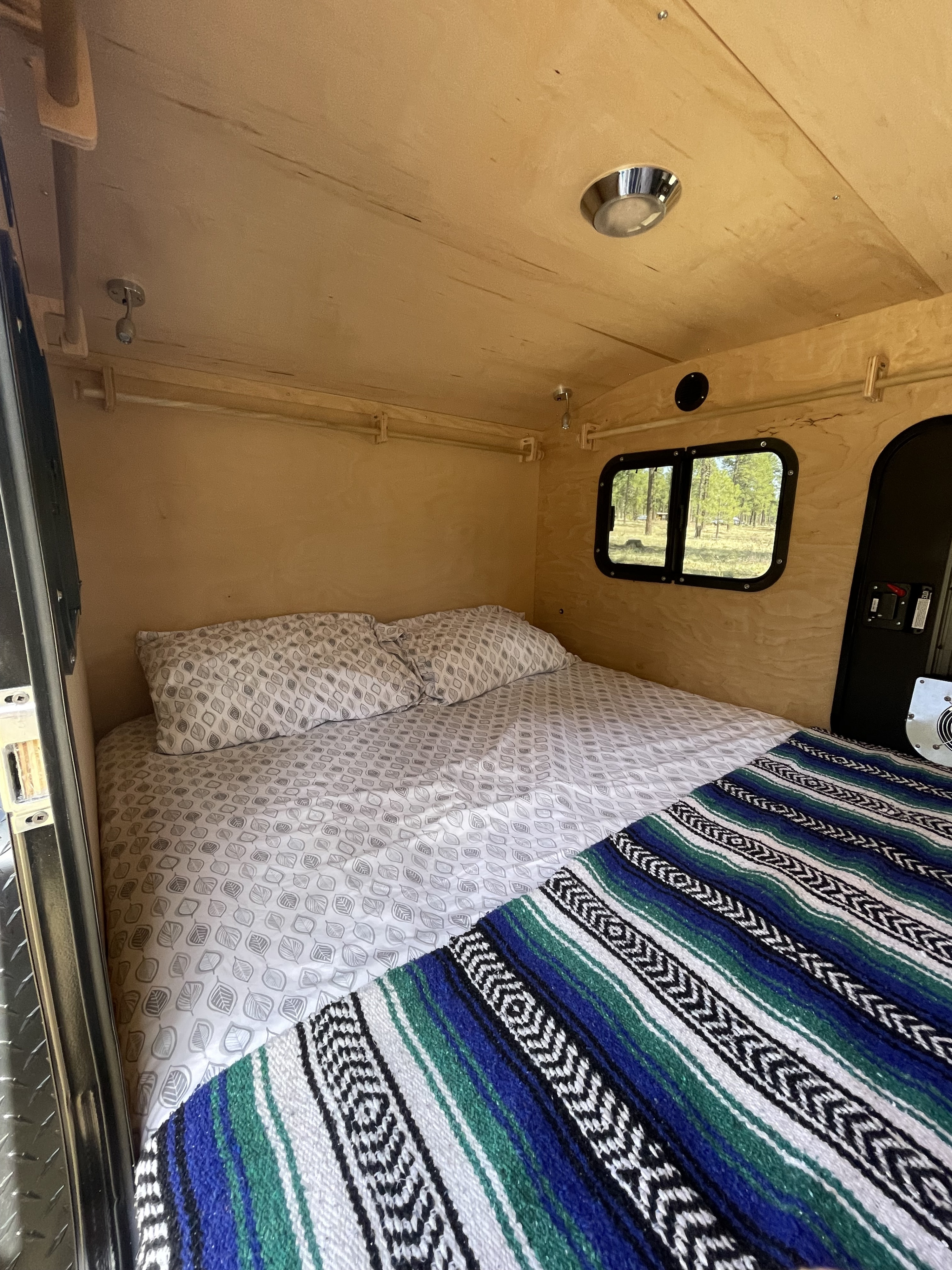 Cozy RV rental interior, featuring a comfortable bed with leaf-patterned sheets, a colorful blanket, and wood paneling.. TC Teardrop Overland 2021
