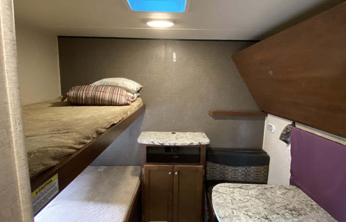 Inside an RV rental: view of a cozy bunk bed area on the left, with a storage cabinet and a small dinette on the right.. Heartland Trail Runner 2017