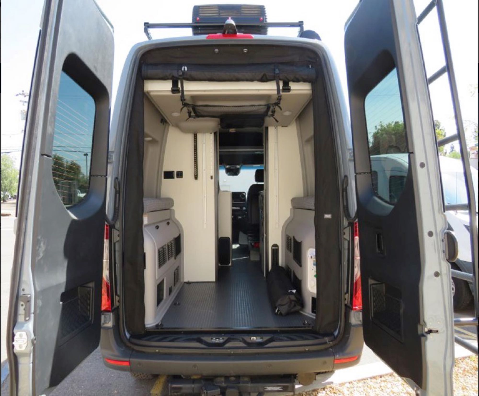 Inside an rv rental camper van: rear view showcasing open doors, adaptable living space with storage, and front cabin.. Winnebago Revel 2022