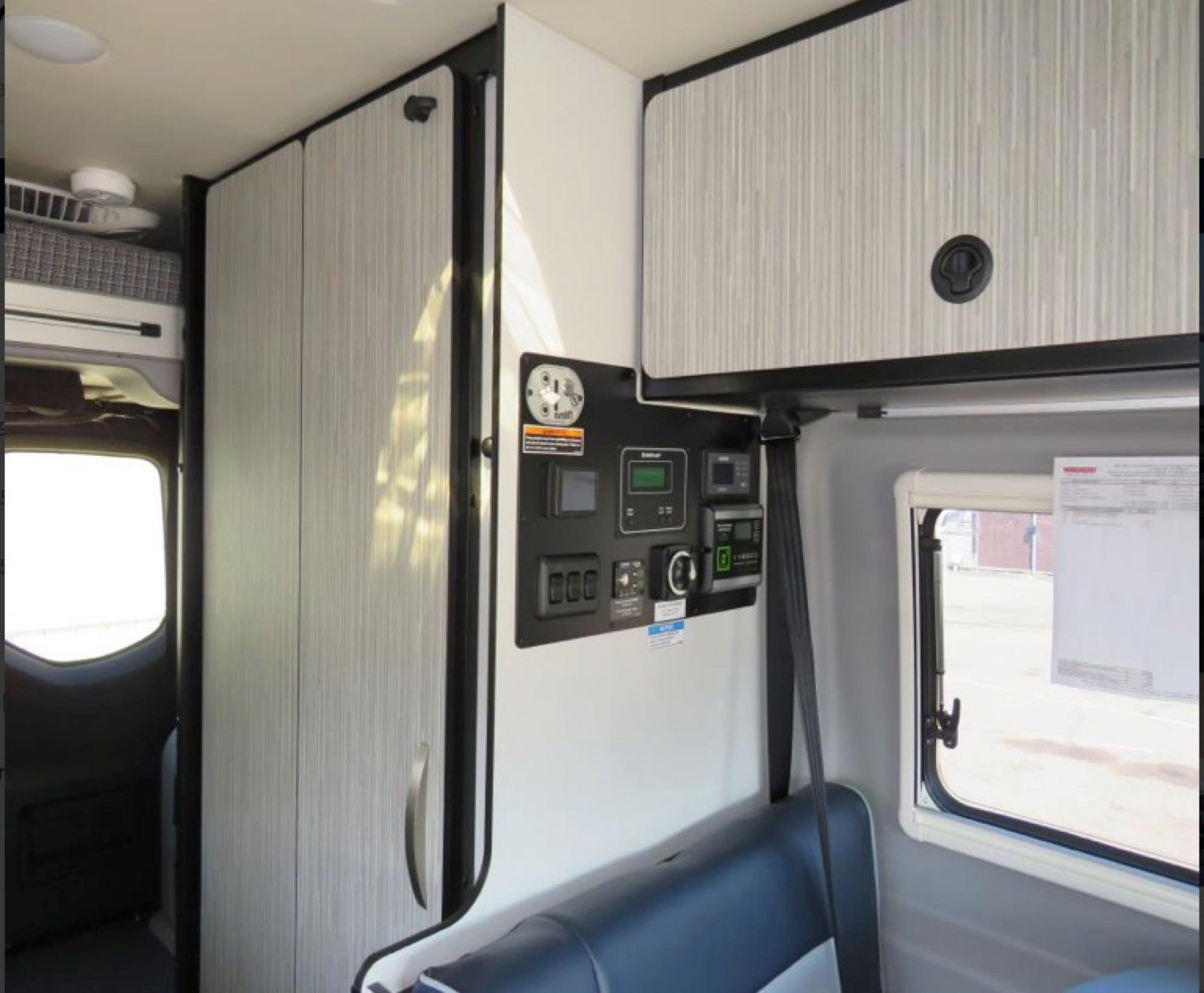 RV rental interior: A central control panel, modern light wood cabinetry with storage, and comfortable blue and gray seating.. Winnebago Revel 2022