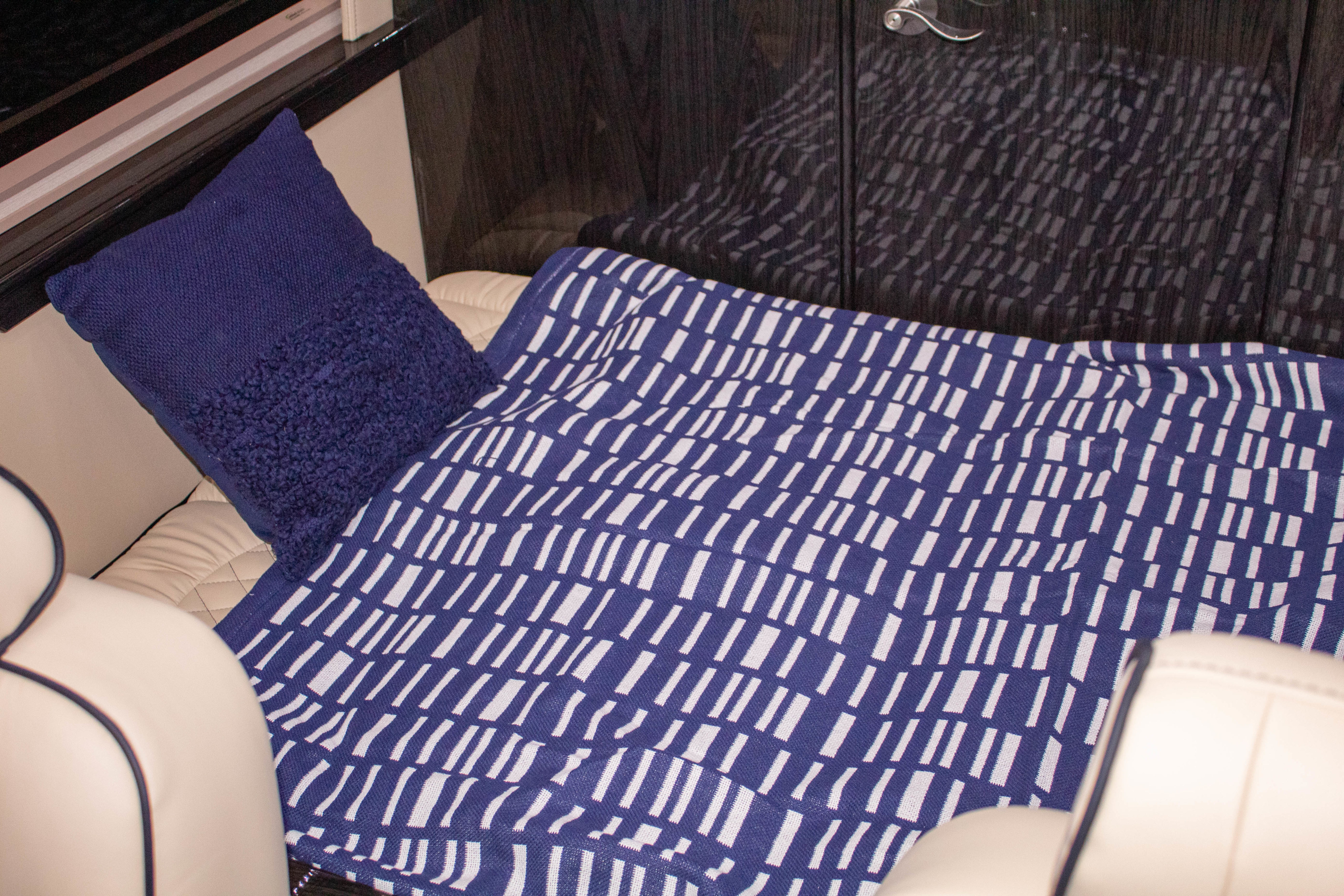 Inside a luxurious RV rental, featuring a cozy blue pillow and a patterned blanket on soft, light-colored seating.. Ultimate Toys Commuter 144 2022