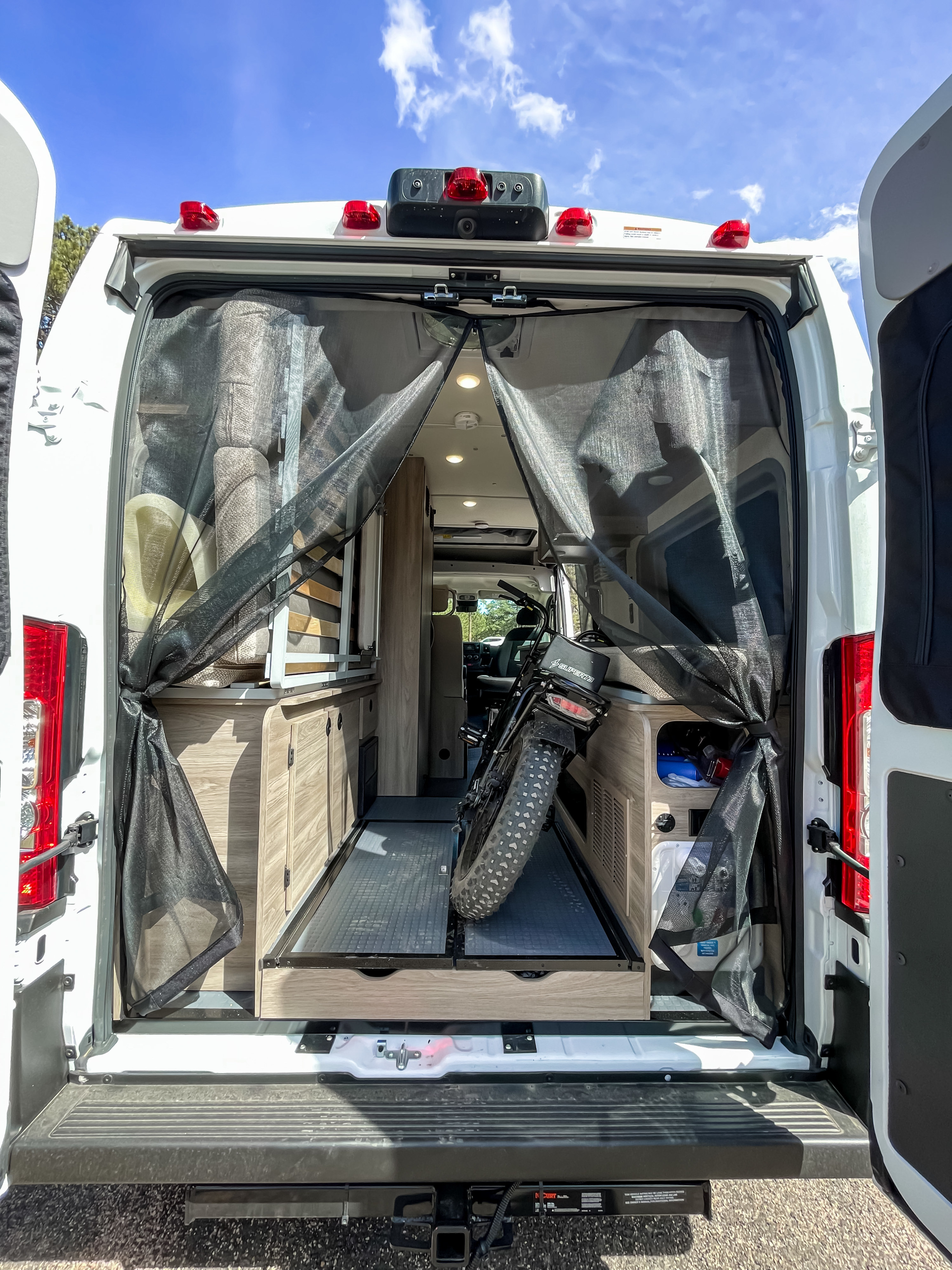 RV rental camper van's rear reveals an e-bike on a pull-out tray, mesh screens, and cabinets, ready for travel.. Winnebago Solis 2022