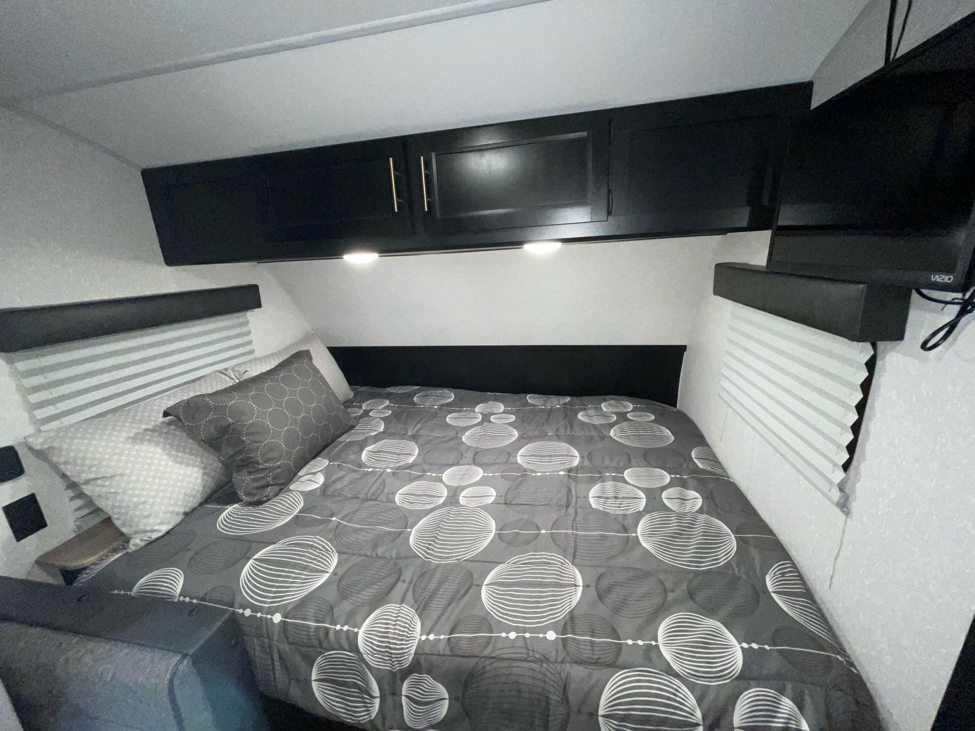 Cozy RV rental bedroom features a bed with grey comforter, black cabinets, and TV.. Forest River Cherokee Wolf Pup 2022