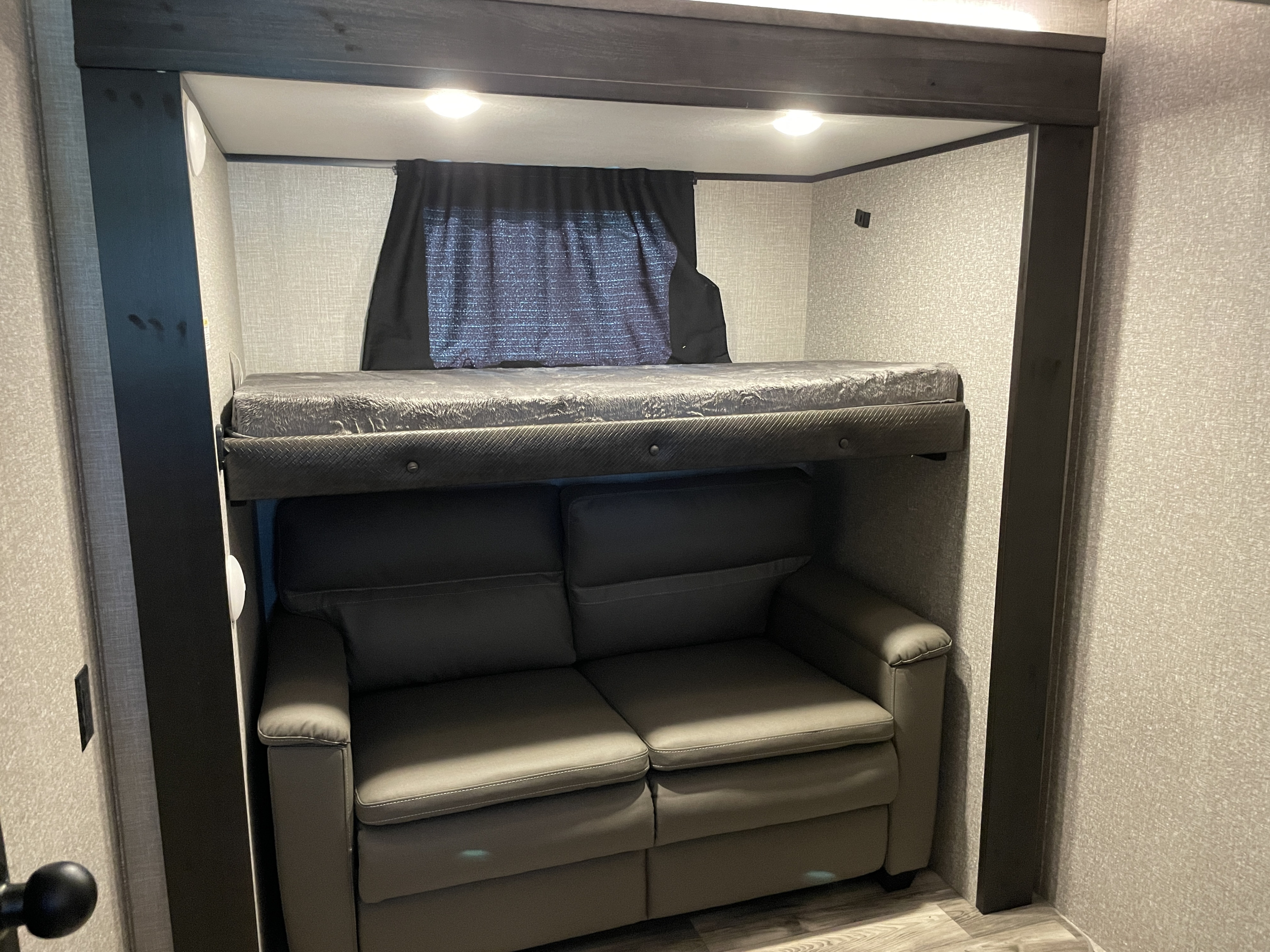 Inside an RV rental, a compact living space shows a dark gray sofa beneath an elevated bunk bed.. Jayco Eagle 2022