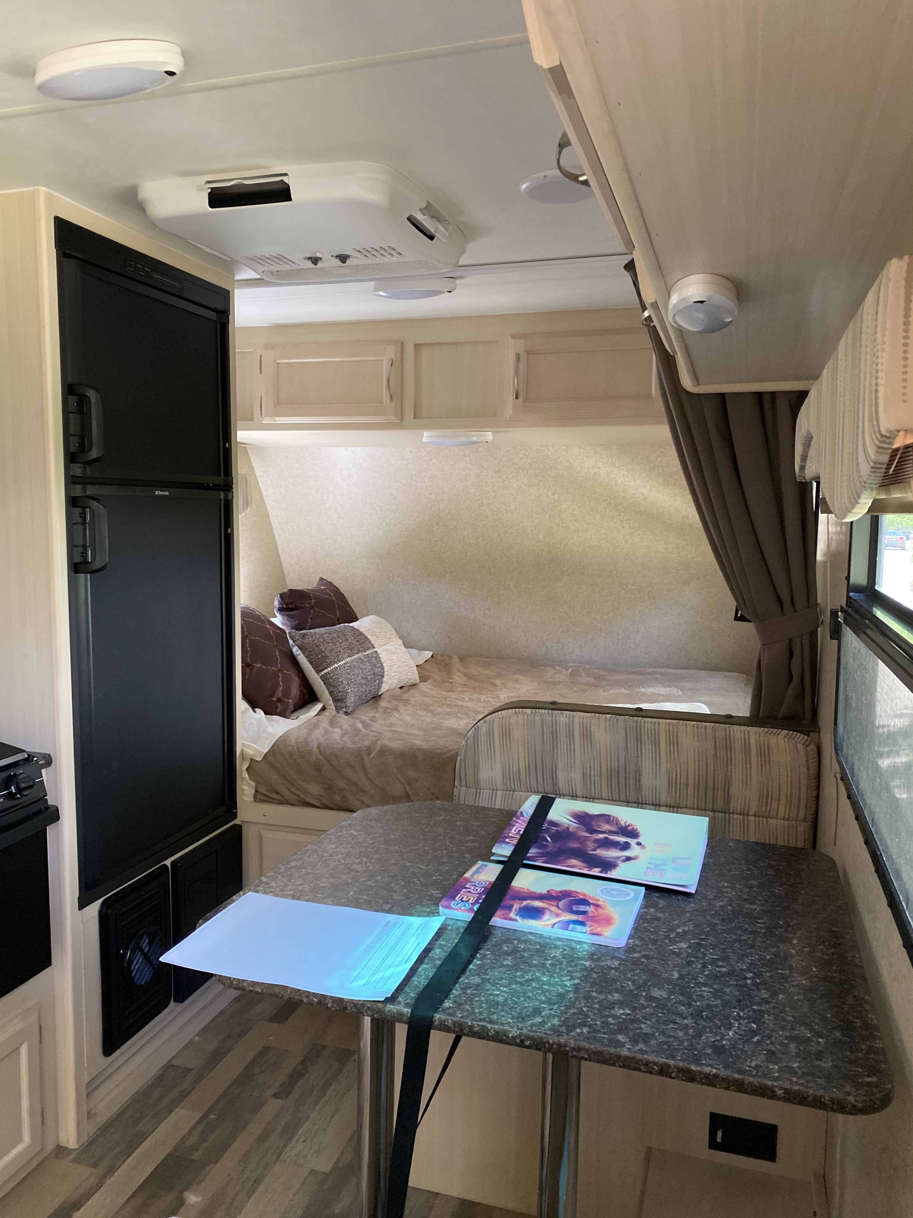 Inside a compact RV rental, showing a bed/dinette, refrigerator, and overhead AC unit for a comfortable trip.. Winnebago Minnie Winnie 2017