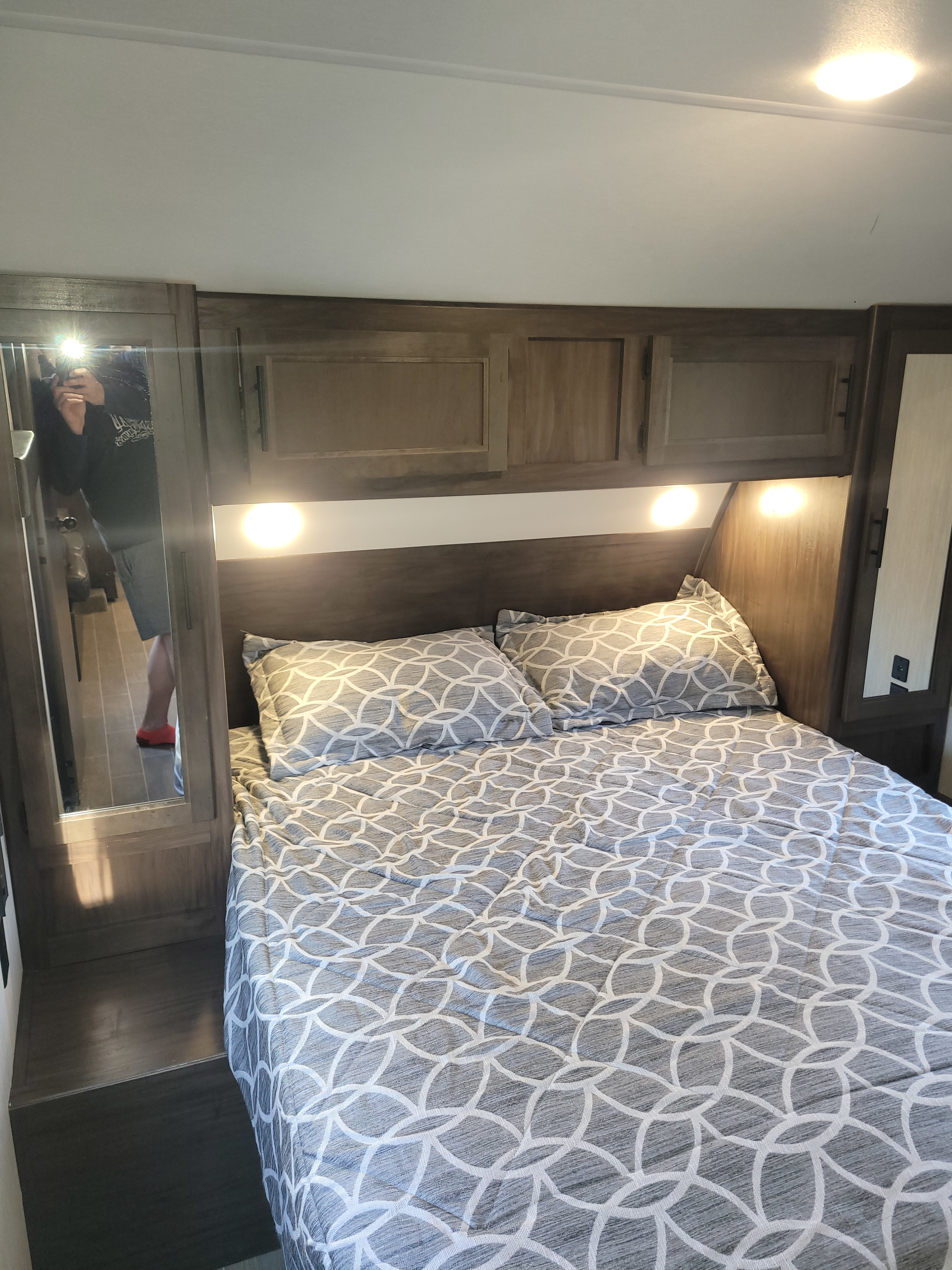 Step into this cozy RV rental bedroom. It features a patterned bed, storage cabinets, and a mirror showing the photographer.. Forest River Cherokee Grey Wolf 2021