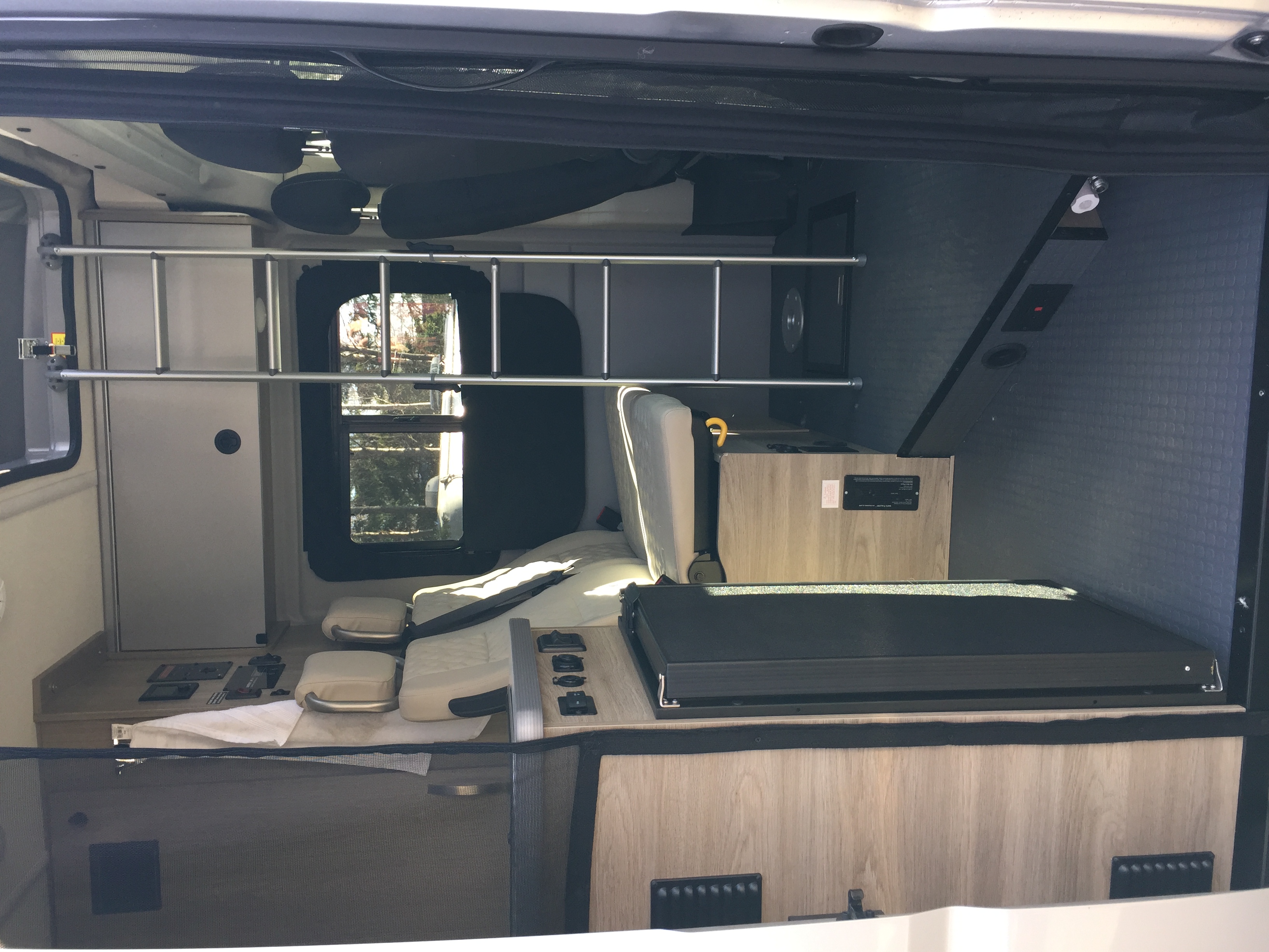Inside an RV rental: compact interior with light seats, wooden cabinetry, windows, and safety bars.. Winnebago Solis 2022