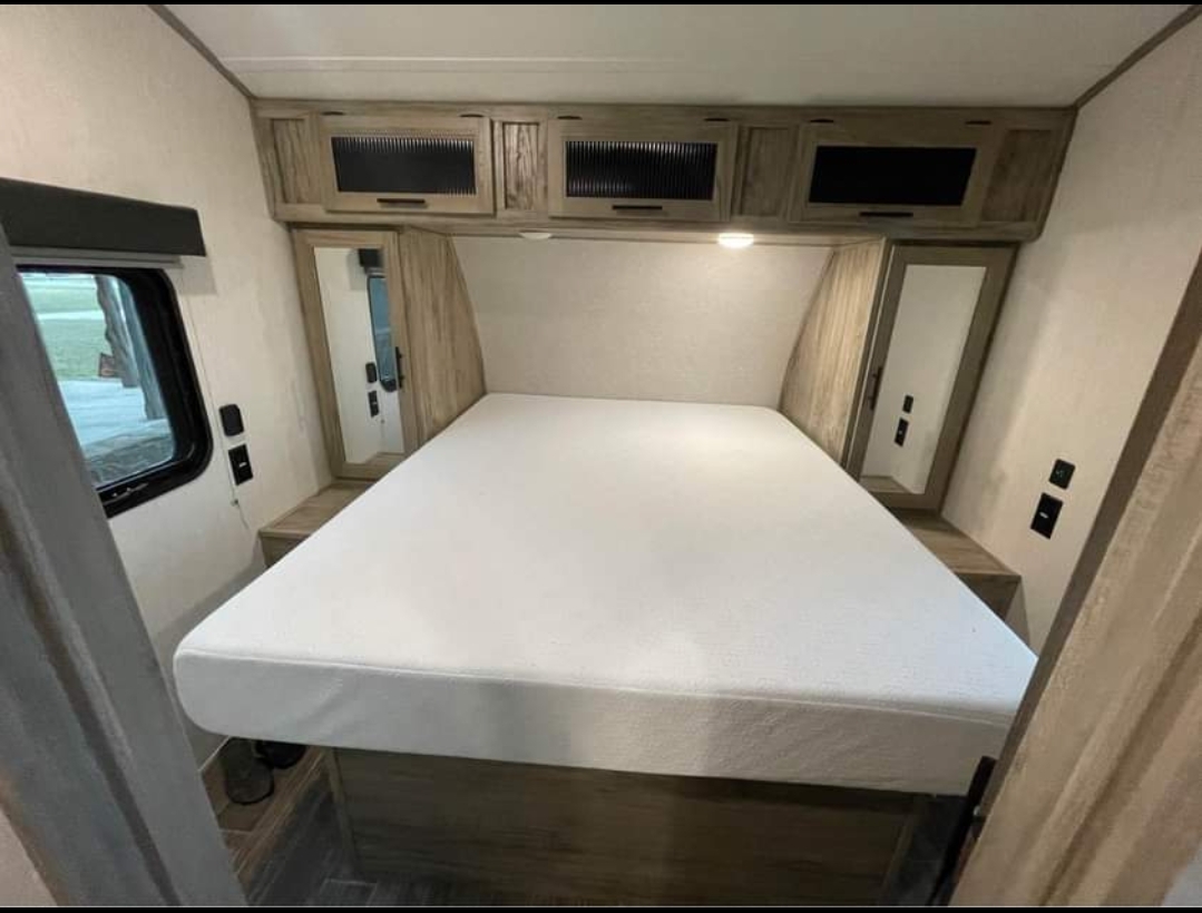 Bright RV rental bedroom: large white mattress, overhead wood-look cabinets, side window, and mirrored wardrobe.. Forest River Cherokee Alpha Wolf 2021