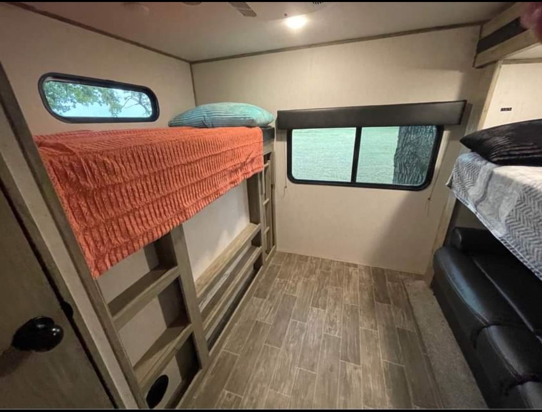 This RV rental features a cozy bunk bed setup with an orange blanket, windows, and a lower couch, ideal for adventures.. Forest River Cherokee Alpha Wolf 2021