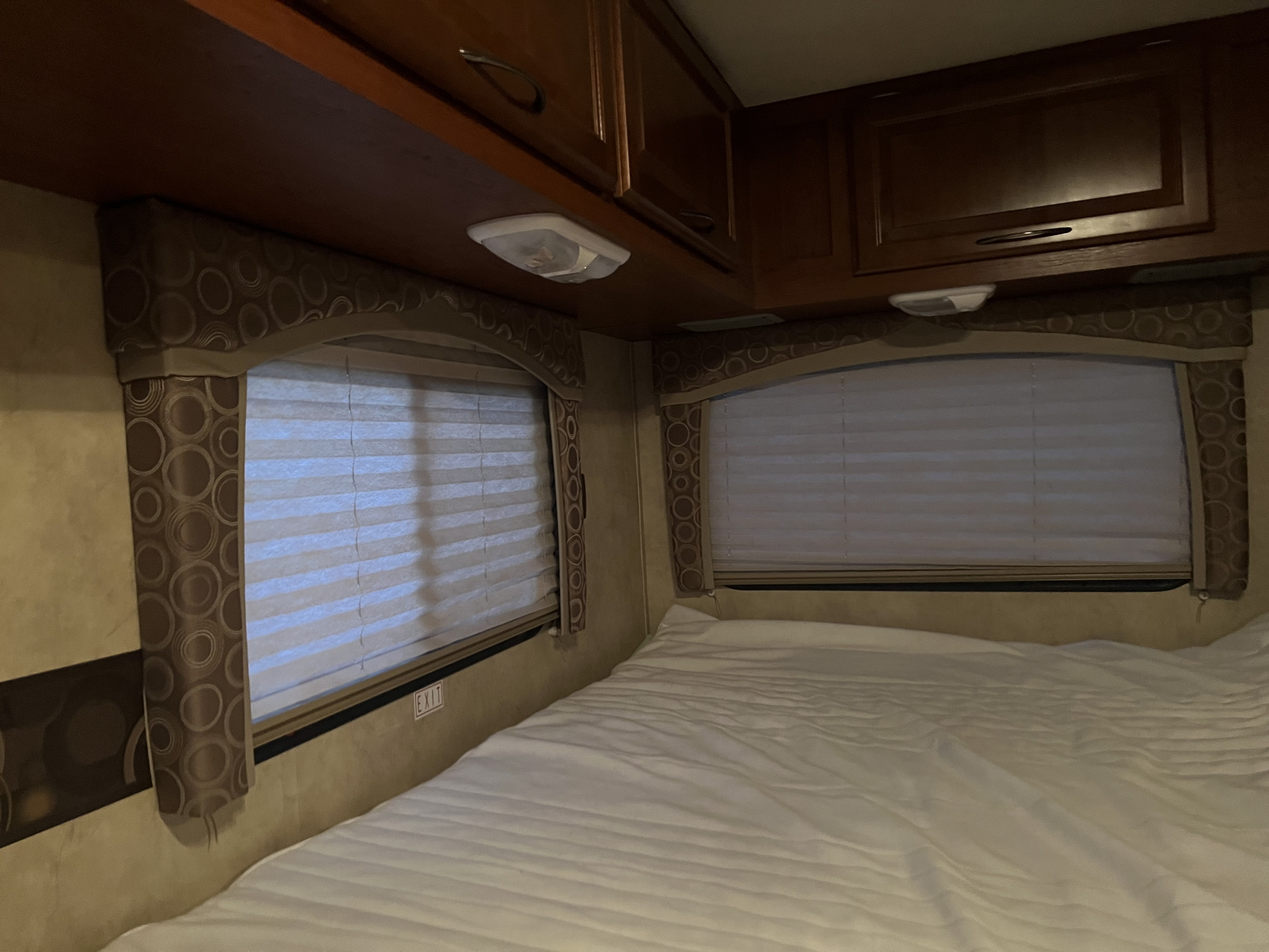 Cozy RV rental bedroom featuring a comfortable bed, windows with blinds, and convenient overhead storage.. Thor Chateau 2012
