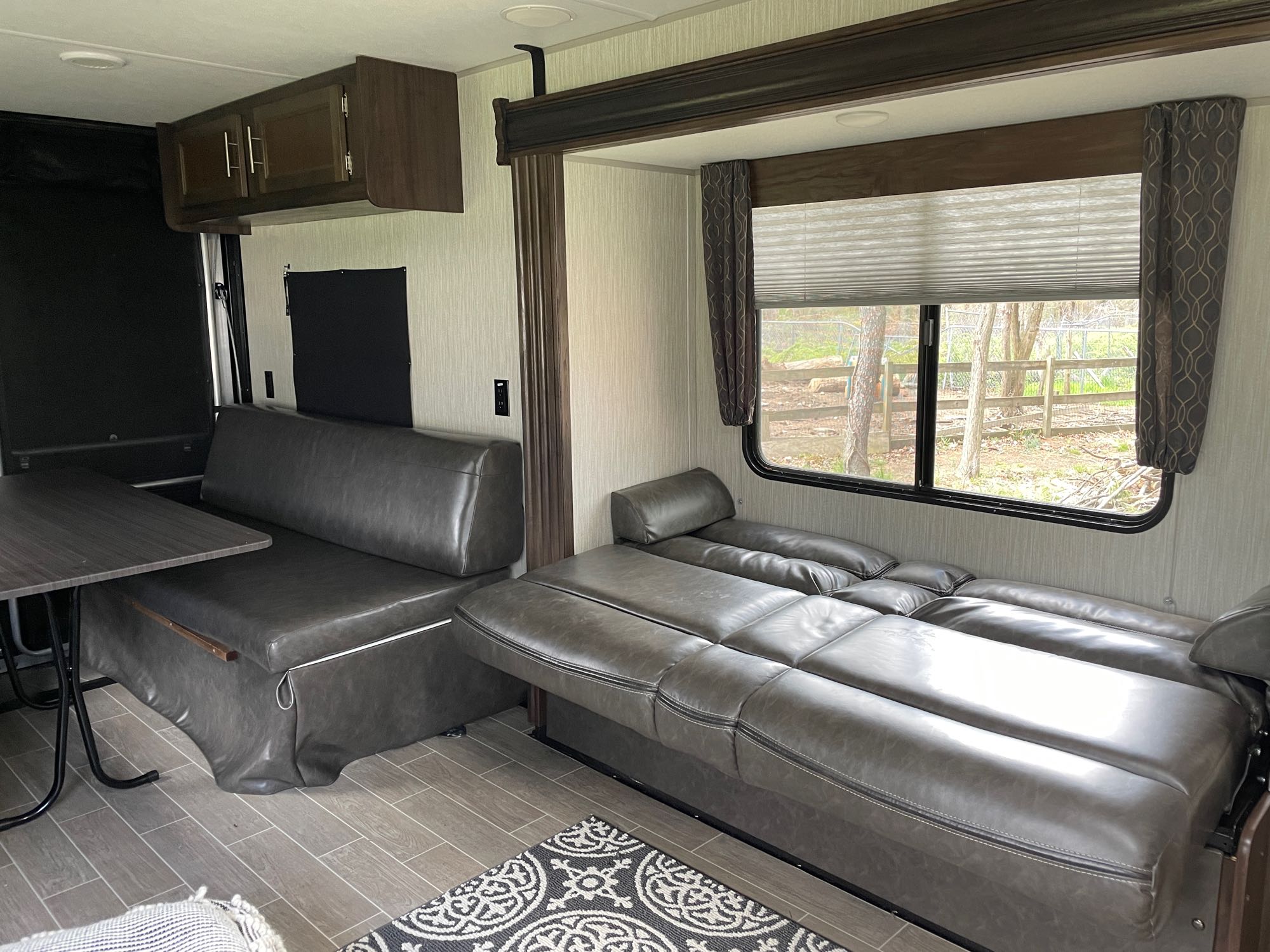 RV rental interior: comfy gray convertible seating, dinette, and window view for a versatile living space.. Forest River Cherokee 2020