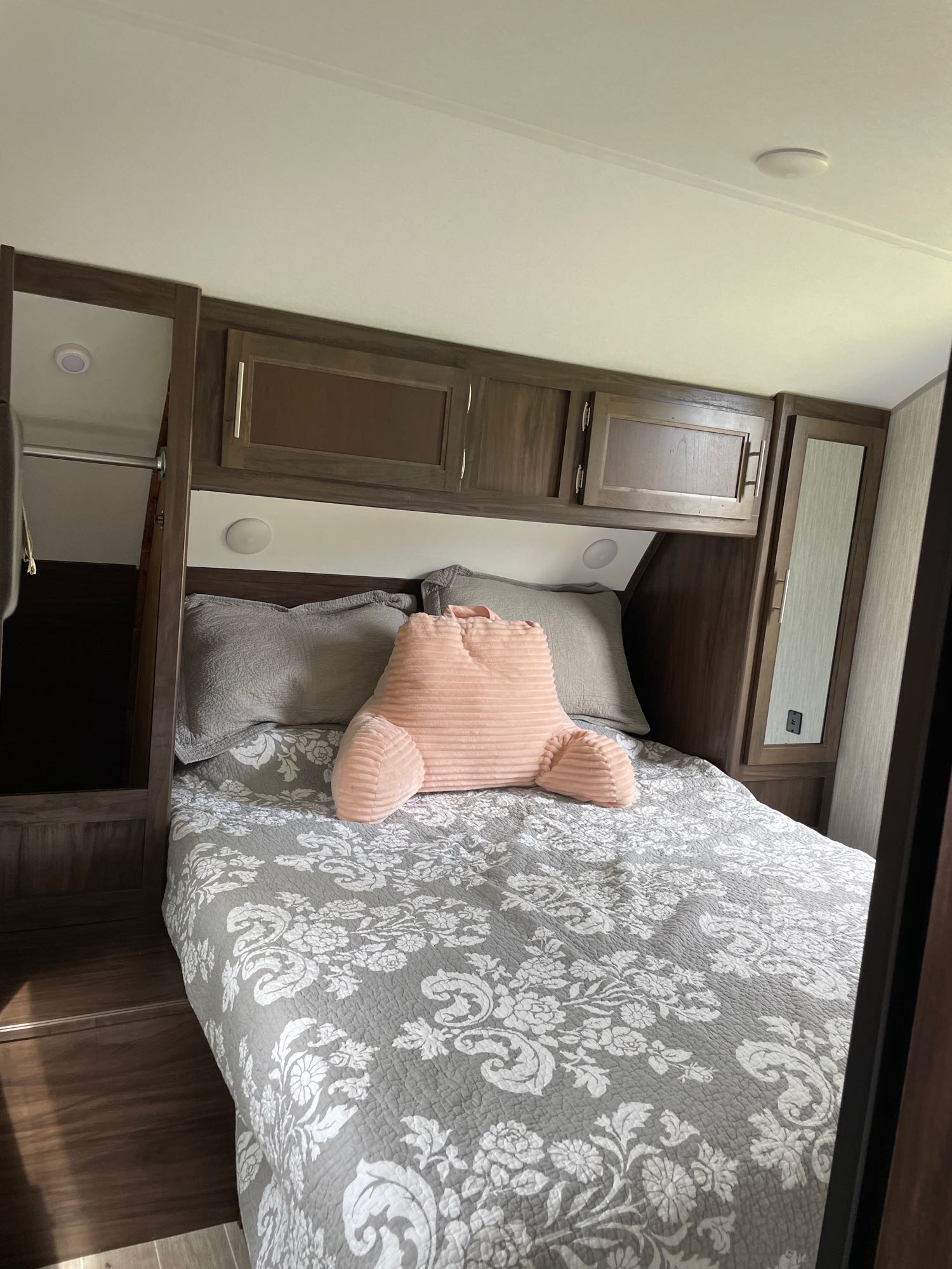 Inside an RV rental: a neat bedroom featuring a bed with a gray floral quilt and a pink reading pillow.. Forest River Cherokee 2020