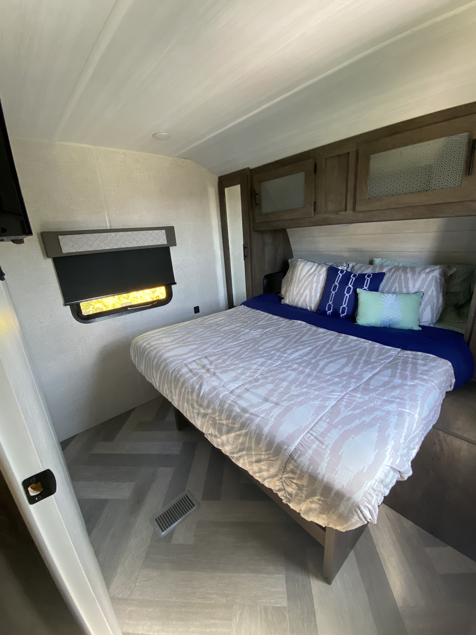 Cozy RV rental bedroom with a bed, patterned bedding, blue sheets, overhead cabinets, and a window.. Forest River Salem 2021