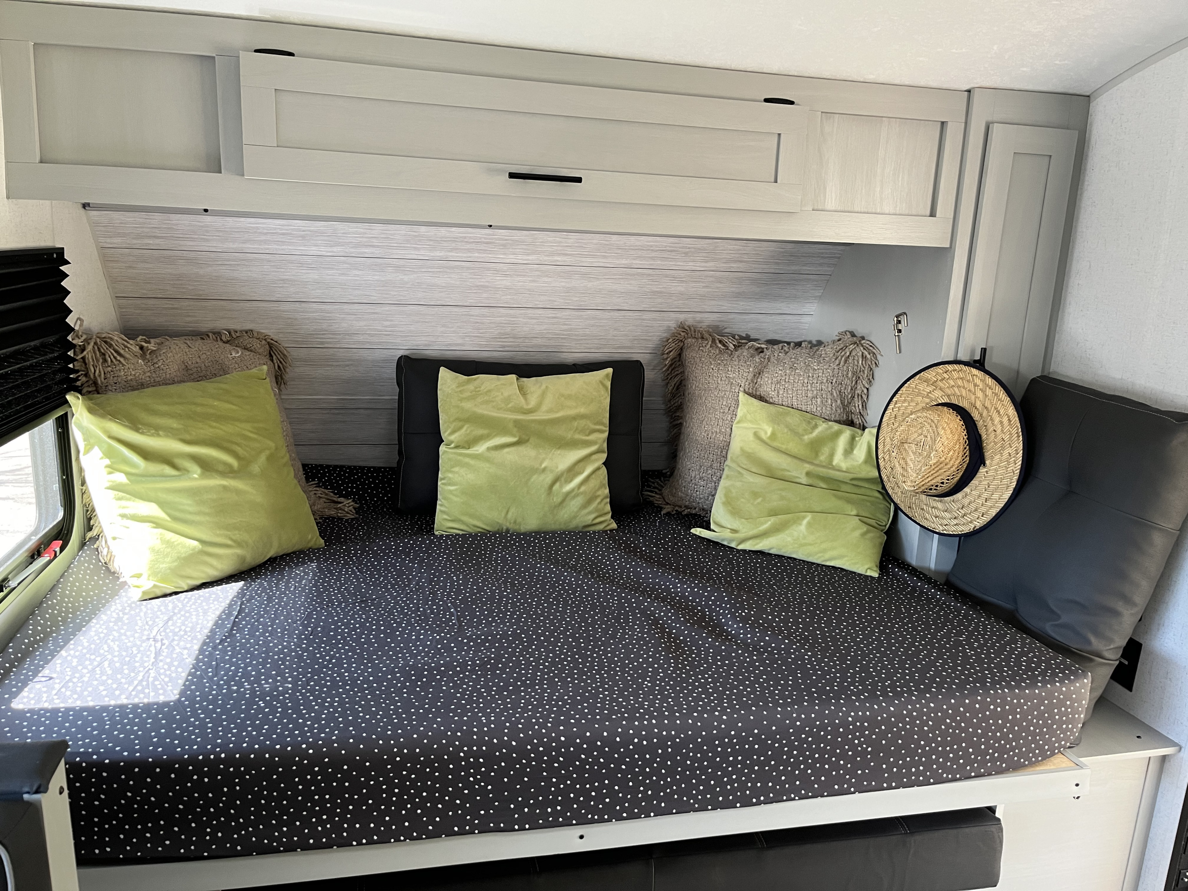 Cozy RV rental bed area with polka dot mattress, lime green and gray pillows, overhead storage, and natural light.. Forest River Wildwood FSX Platinum 2021