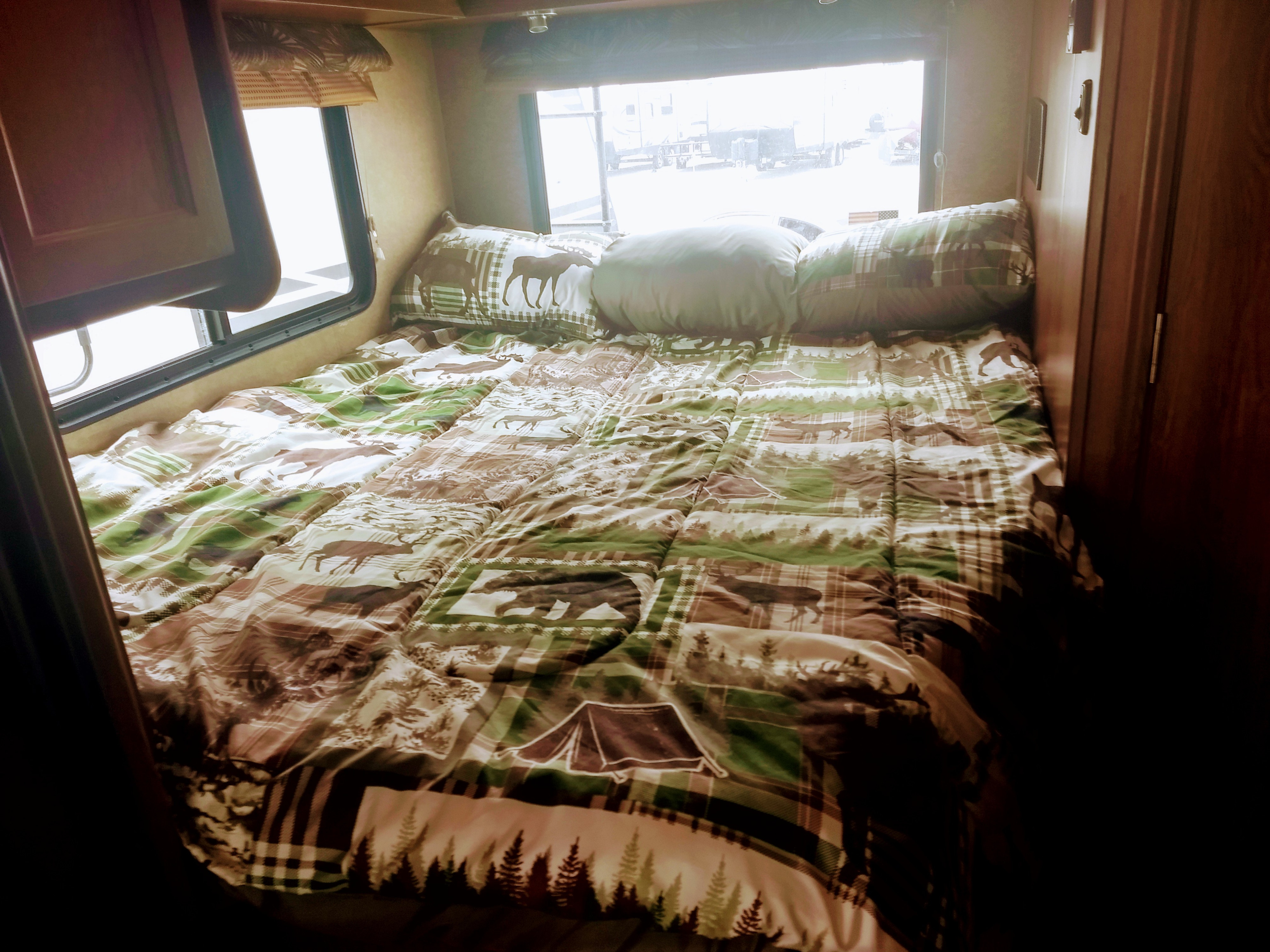 Inviting RV rental sleeping area with forest & animal print bedding by windows, perfect for nature lovers.. Coachmen Leprechaun 2015