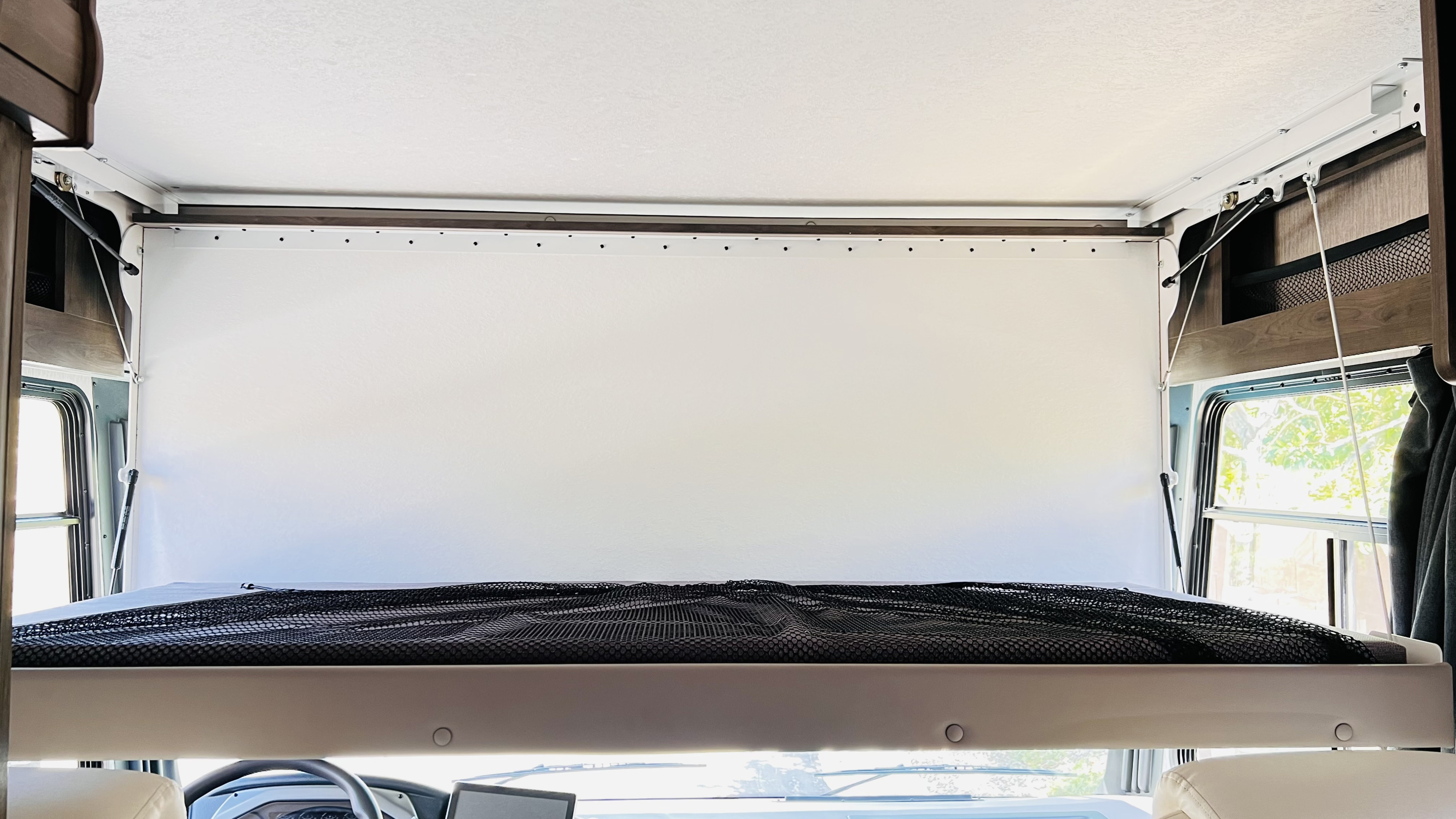 An RV rental's front overhead bunk bed features a black safety net and white head panel, with the cockpit below.. Forest River Coachmen Pursuit 2022