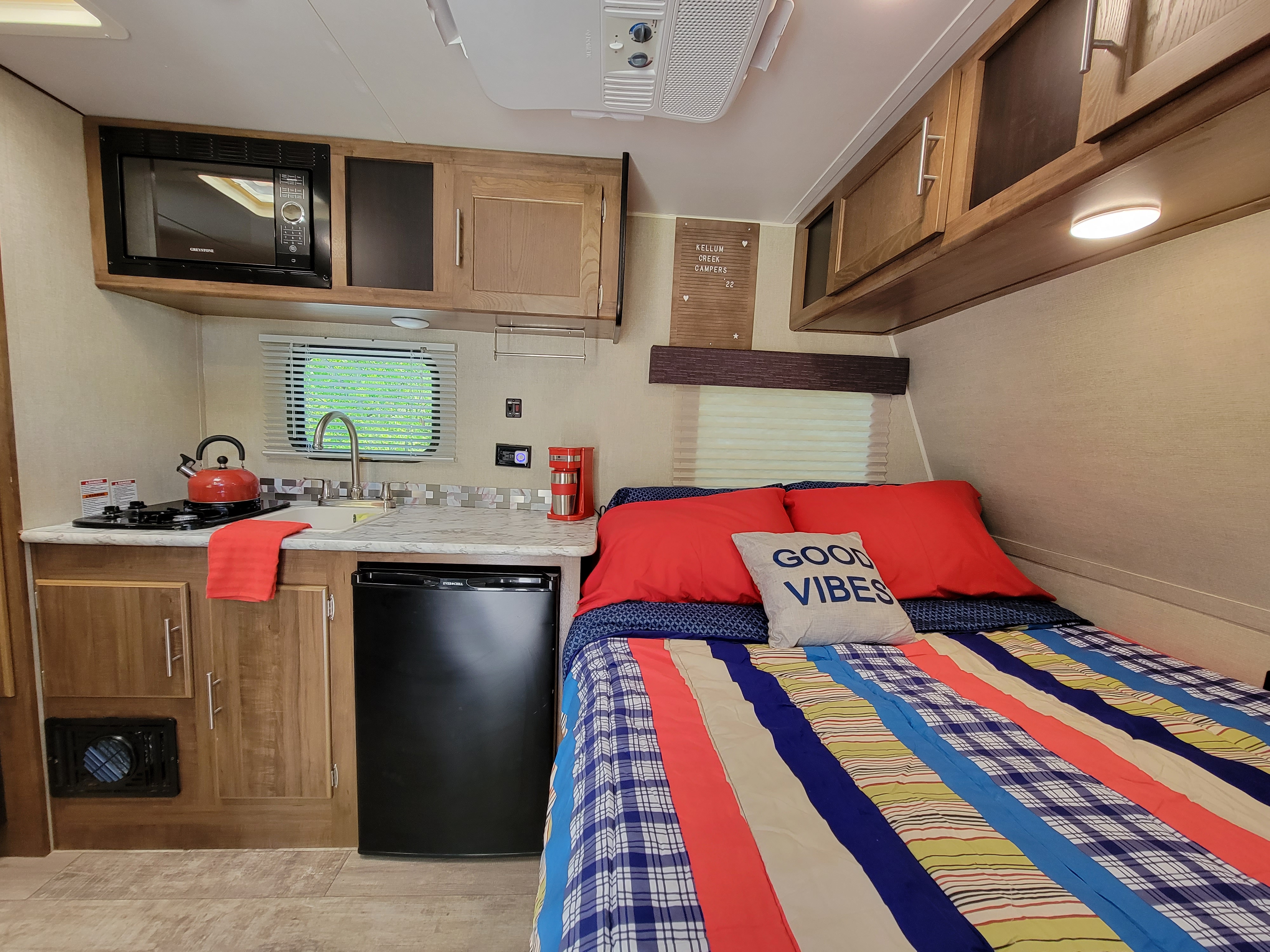 Cozy RV rental interior with compact kitchen (microwave, stove, sink, mini-fridge) and a bed with "Good Vibes" pillow.. Gulf Stream Ameri-Lite Super Lite 2019