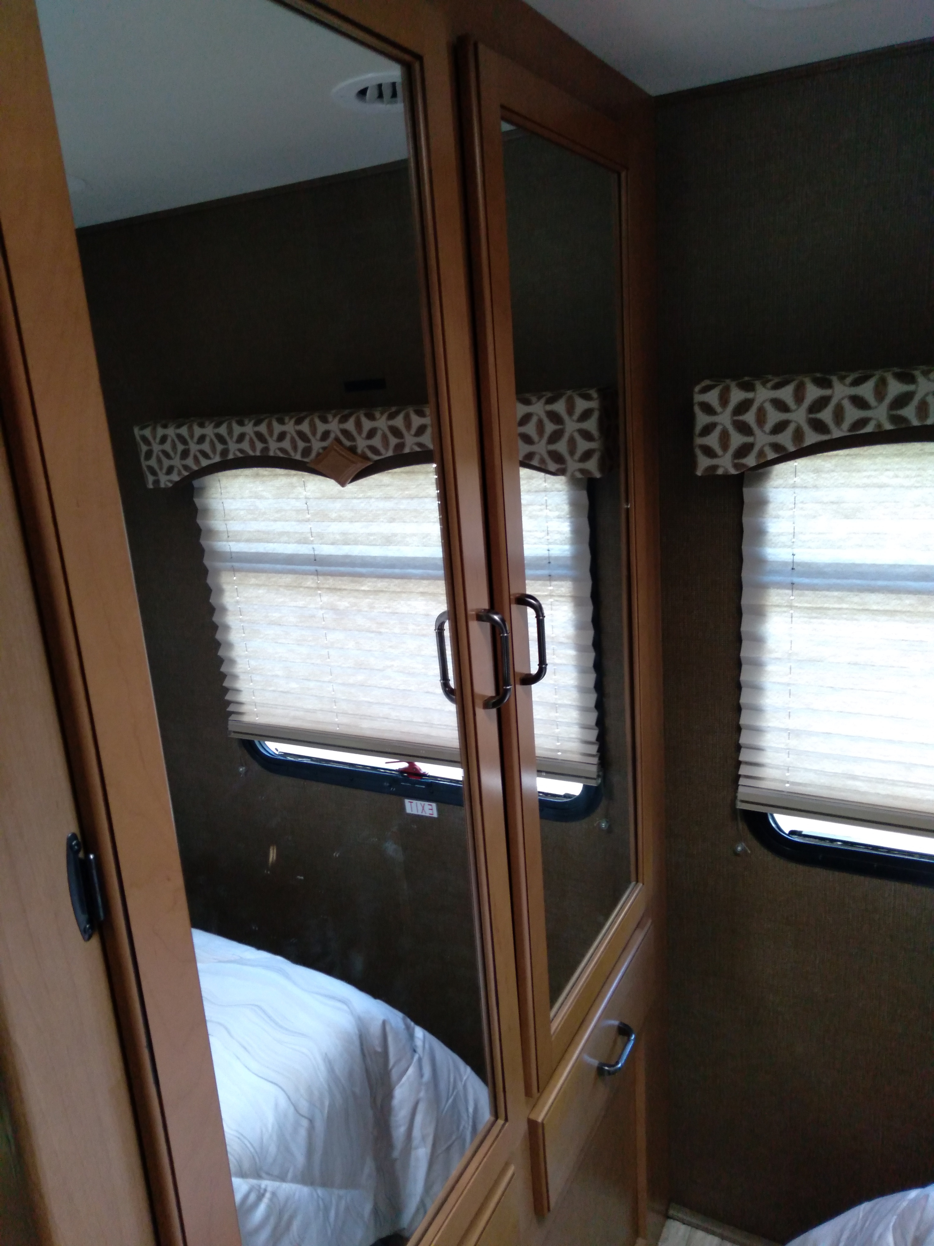 Explore this RV rental bedroom's mirrored closet, comfy bed reflection, and two windows with pleated blinds.. Thor Hurricane 2016