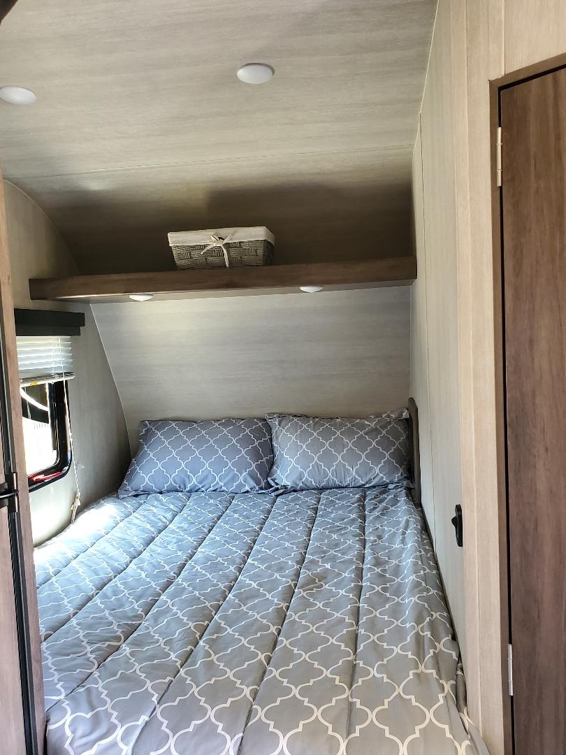 Inside a cozy RV rental: a comfortable bed with gray patterned bedding, overhead shelf & lighting.. Pacific Coachworks Blaze'N 2022