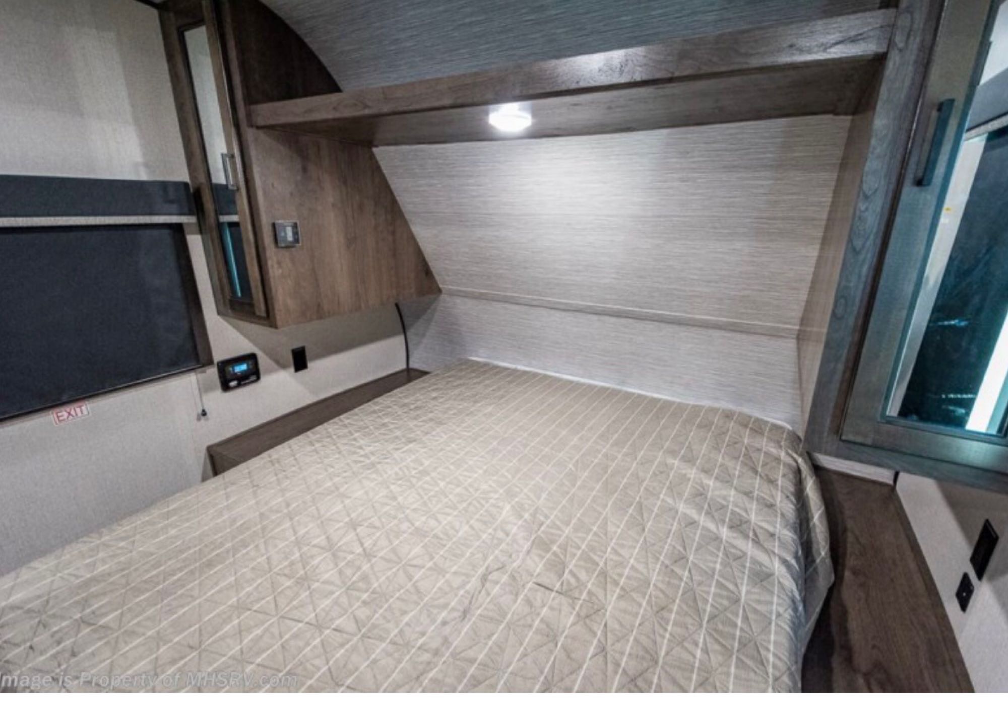 Inside an RV rental: a neat, compact bedroom with a quilted bed, wood cabinets, and functional lighting.. Highland Ridge Olympia 26BHS 2022