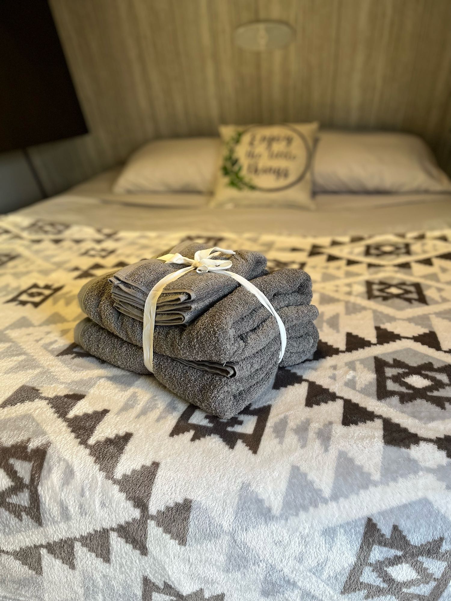 Experience comfort in our RV rental! Cozy bed with patterned blanket, stacked towels, and "Enjoy" pillow awaits your stay.. Pioneer Travel Trailer 2021