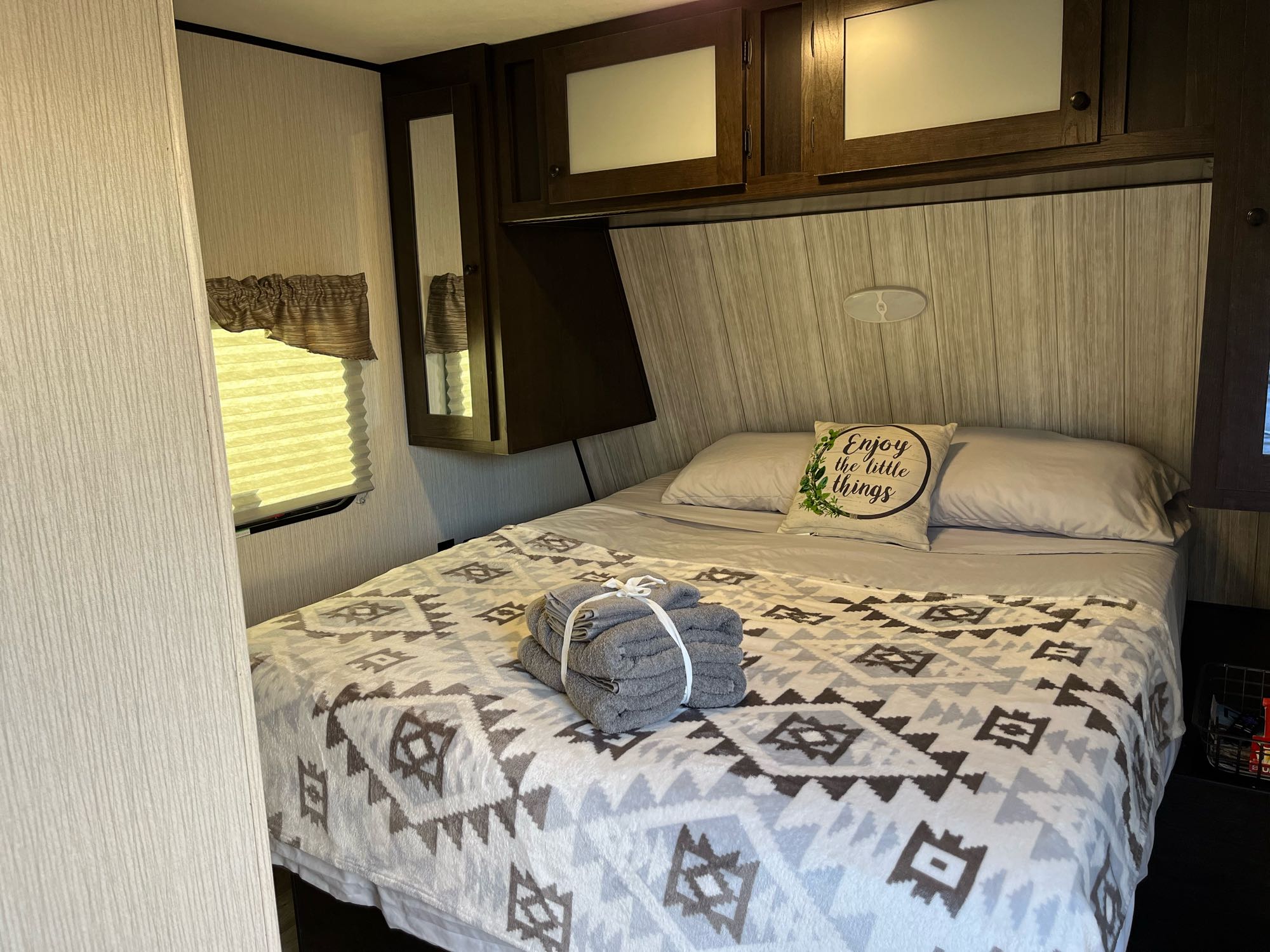 Inside a comfy RV rental bedroom: bed with decorative blanket, fresh towels, and overhead storage.. Pioneer Travel Trailer 2021