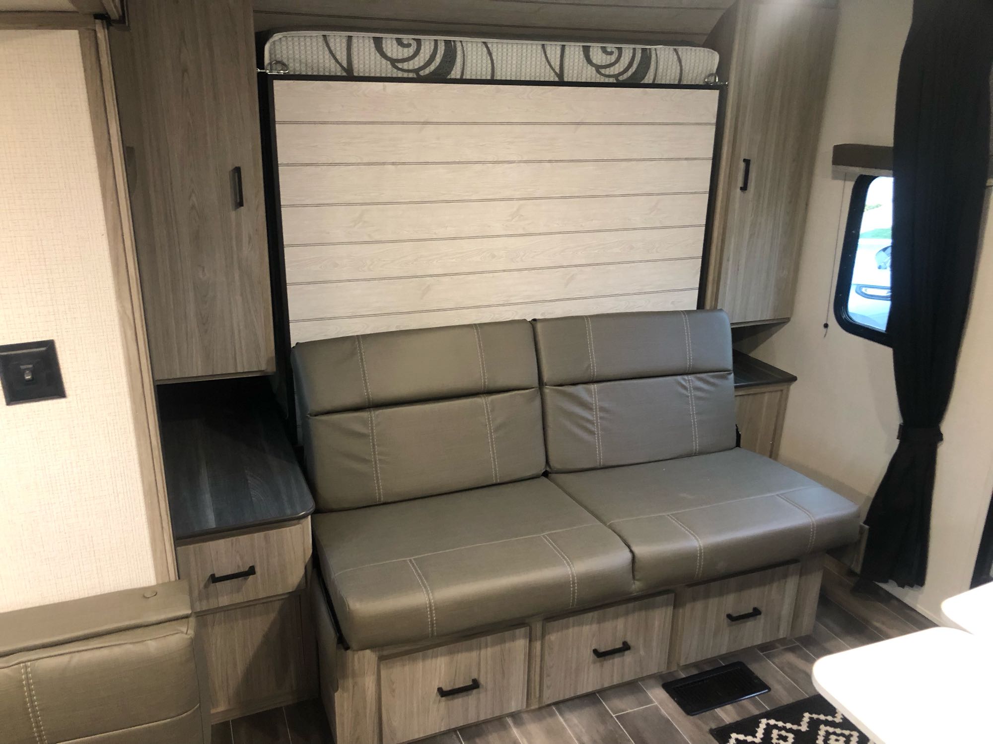 An RV rental features a pull-down bed over a gray sofa with storage drawers, maximizing space in this modern interior.. Other Passport 2022