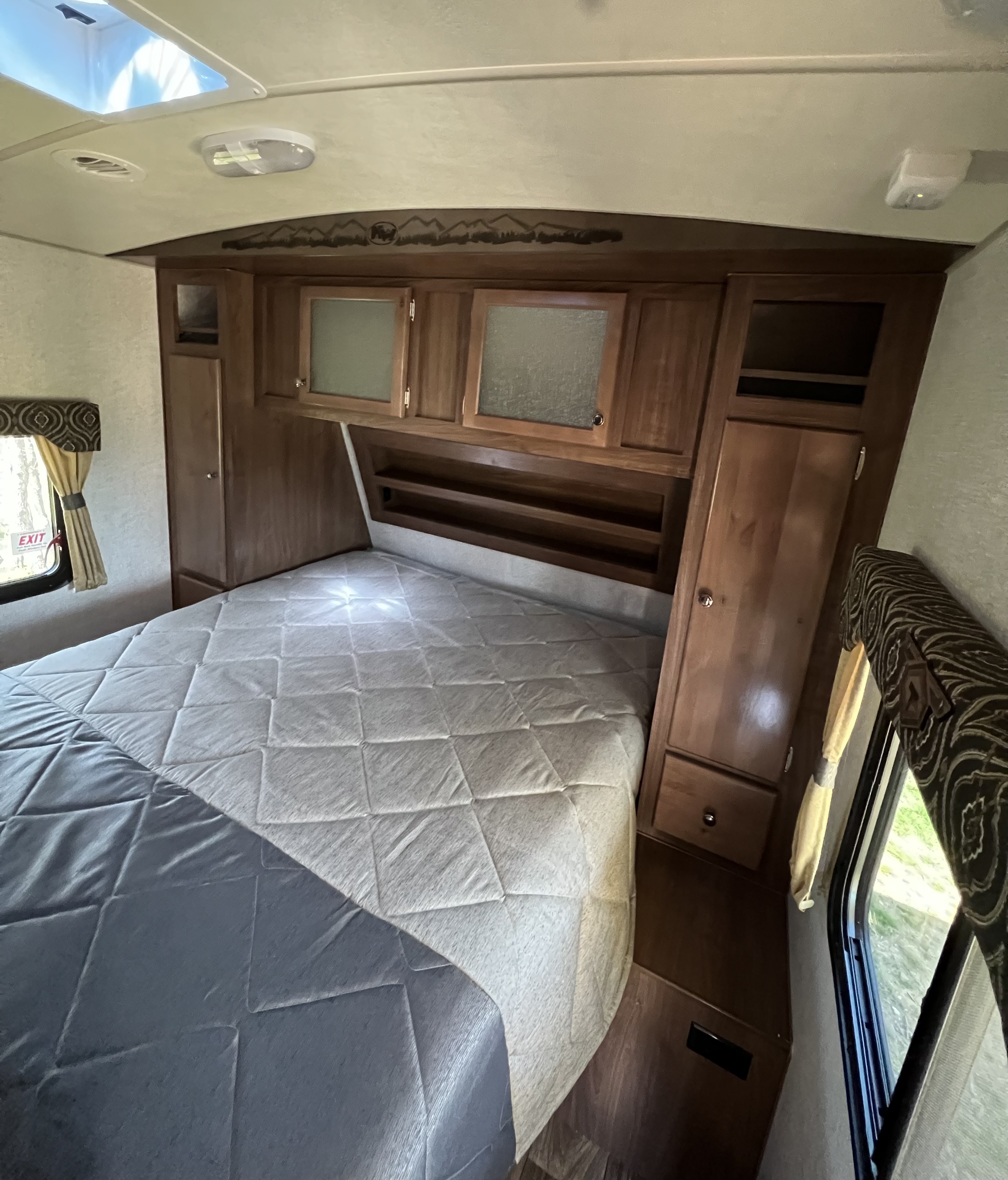 Inside an RV rental bedroom: a comfortable queen bed, ample storage, and bright natural light from windows.. Nash Nash Trailer 2022