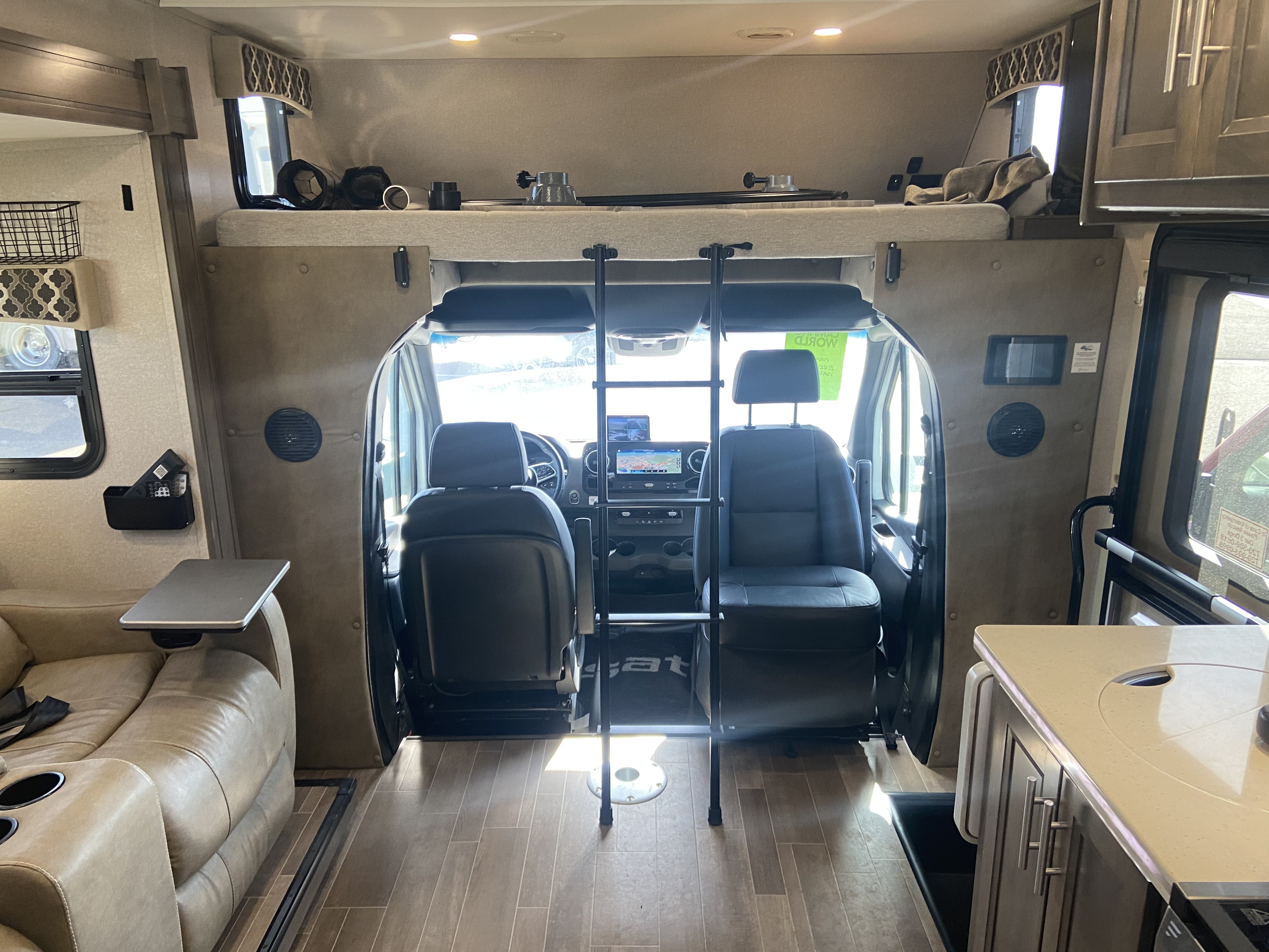 Inside a roomy RV rental: a cozy cab-over bed, driver's cockpit, and a comfy living space with a sofa and table.. Dynamax ISATA 3 2020