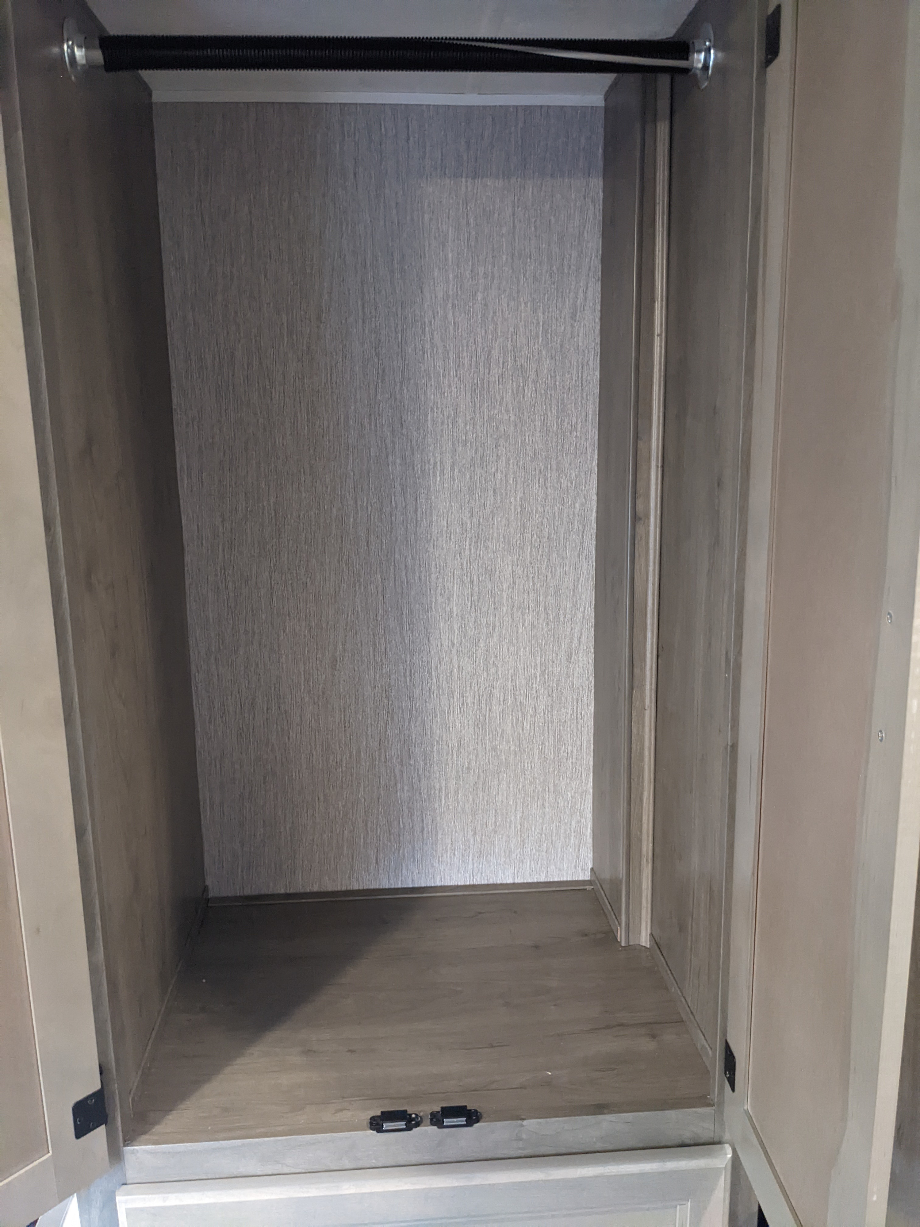 Empty RV rental wardrobe/closet with a clothes rod and wood-grain interior. Two small latches secure the base.. Coachmen Freelander 2021