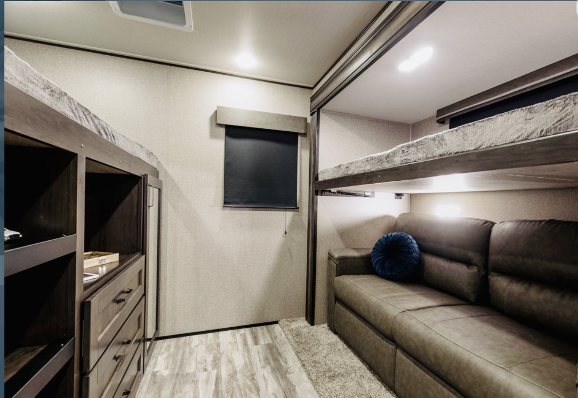 Inside an RV rental: view of a cozy bunk bed area with sofa and storage for comfortable travel.. Grand Design Reflection 2021