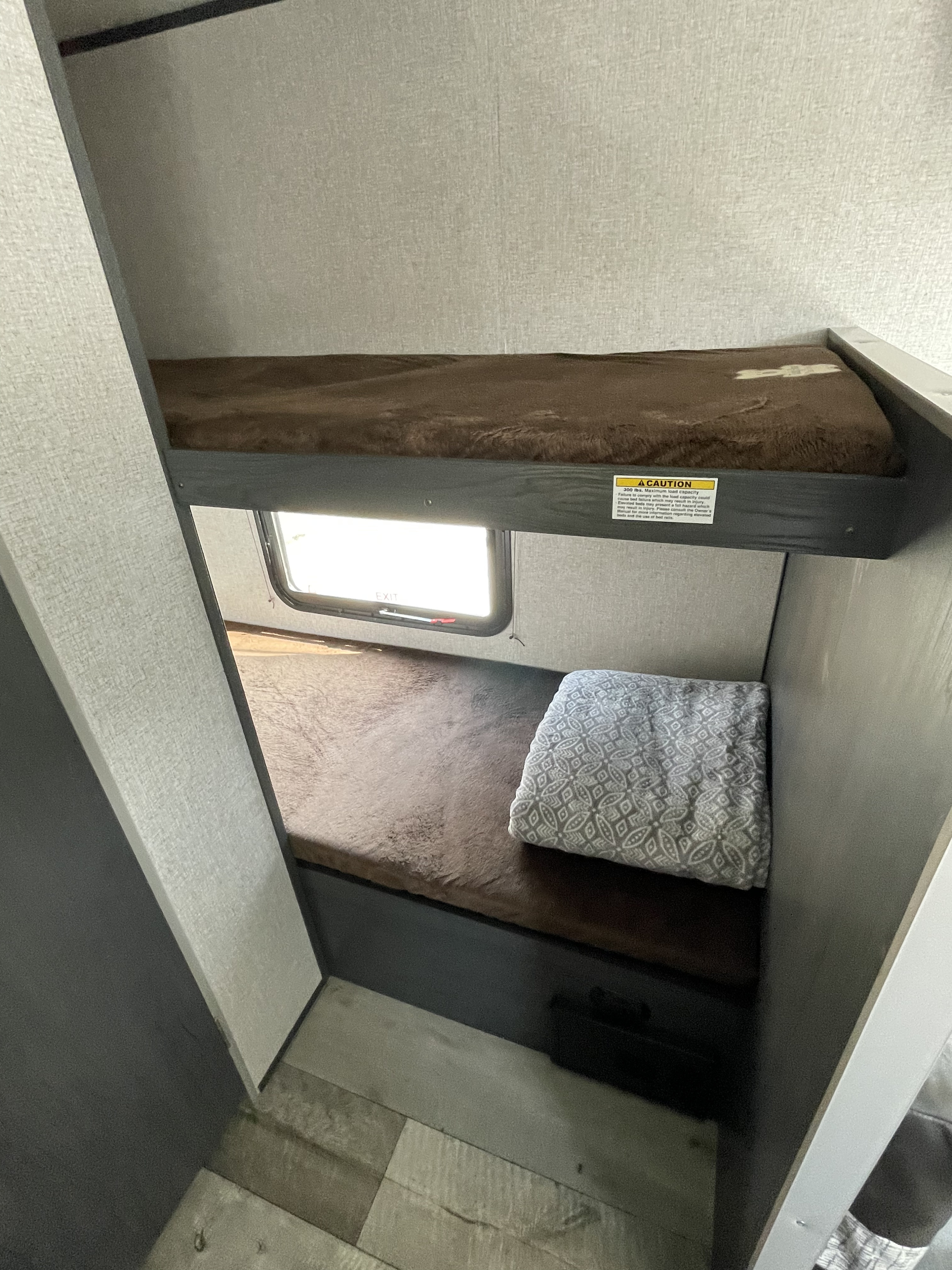RV rental interior featuring cozy bunk beds with brown coverings. The top bunk has a 300 lbs. load capacity warning.. Aspen Trail LE 2021