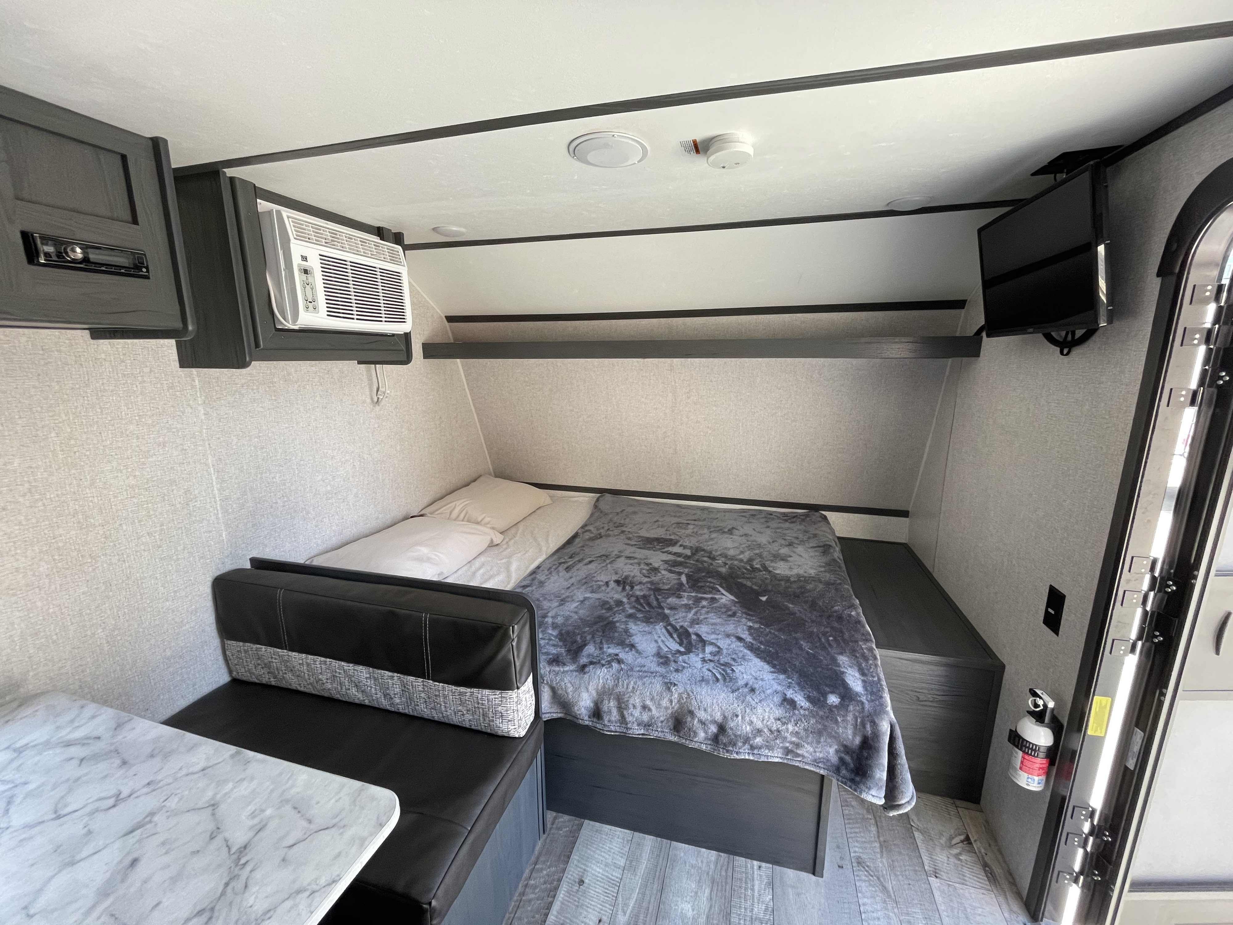 This cozy rv rental showcases a compact bedroom area with a bed, TV, AC, and a small dinette.. Aspen Trail LE 2021