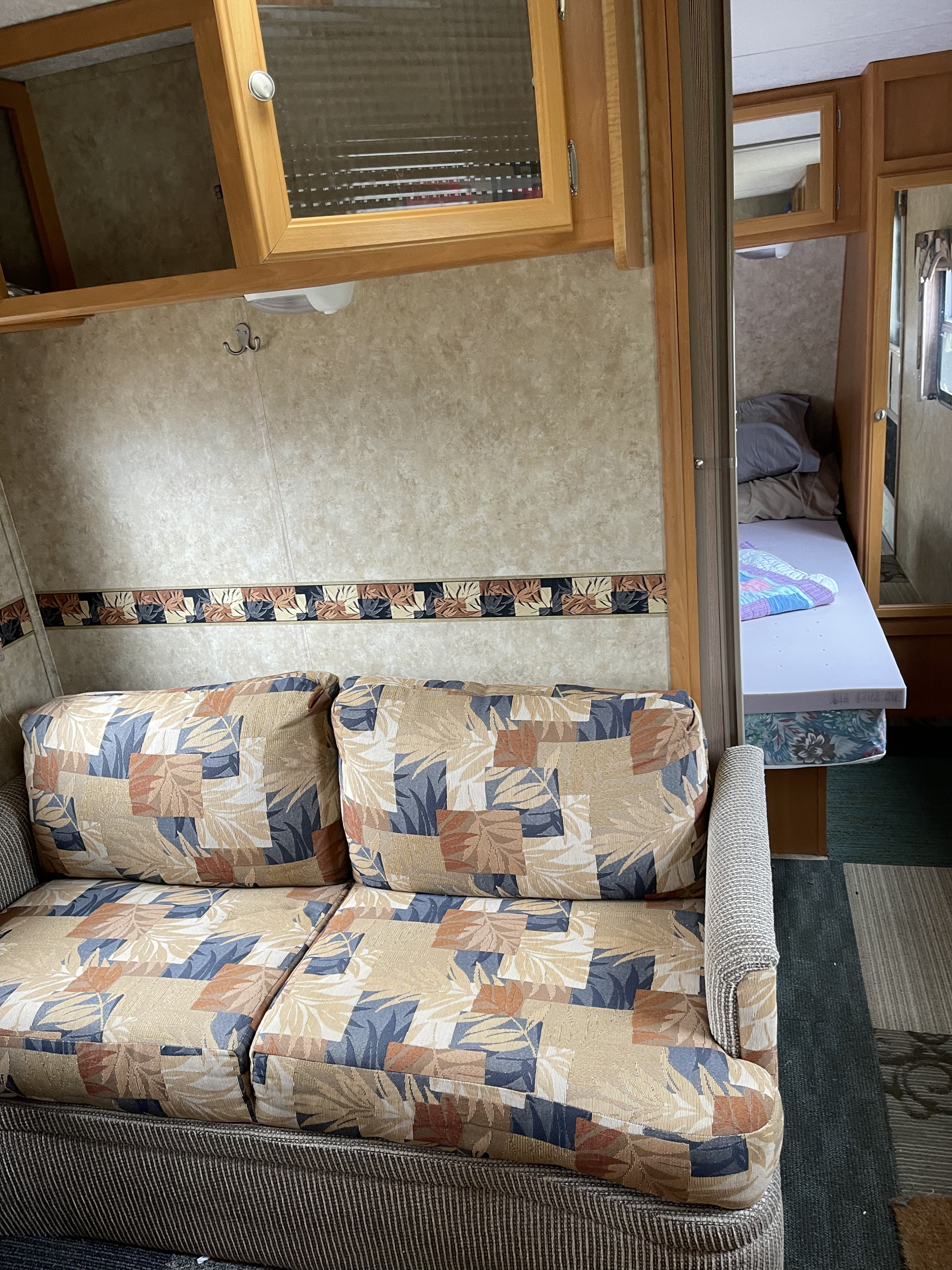 Cozy RV rental interior featuring a patterned sofa, overhead cabinets, and a peek at a bunk bed area.. Pilgrim Route 66 flyer 2007