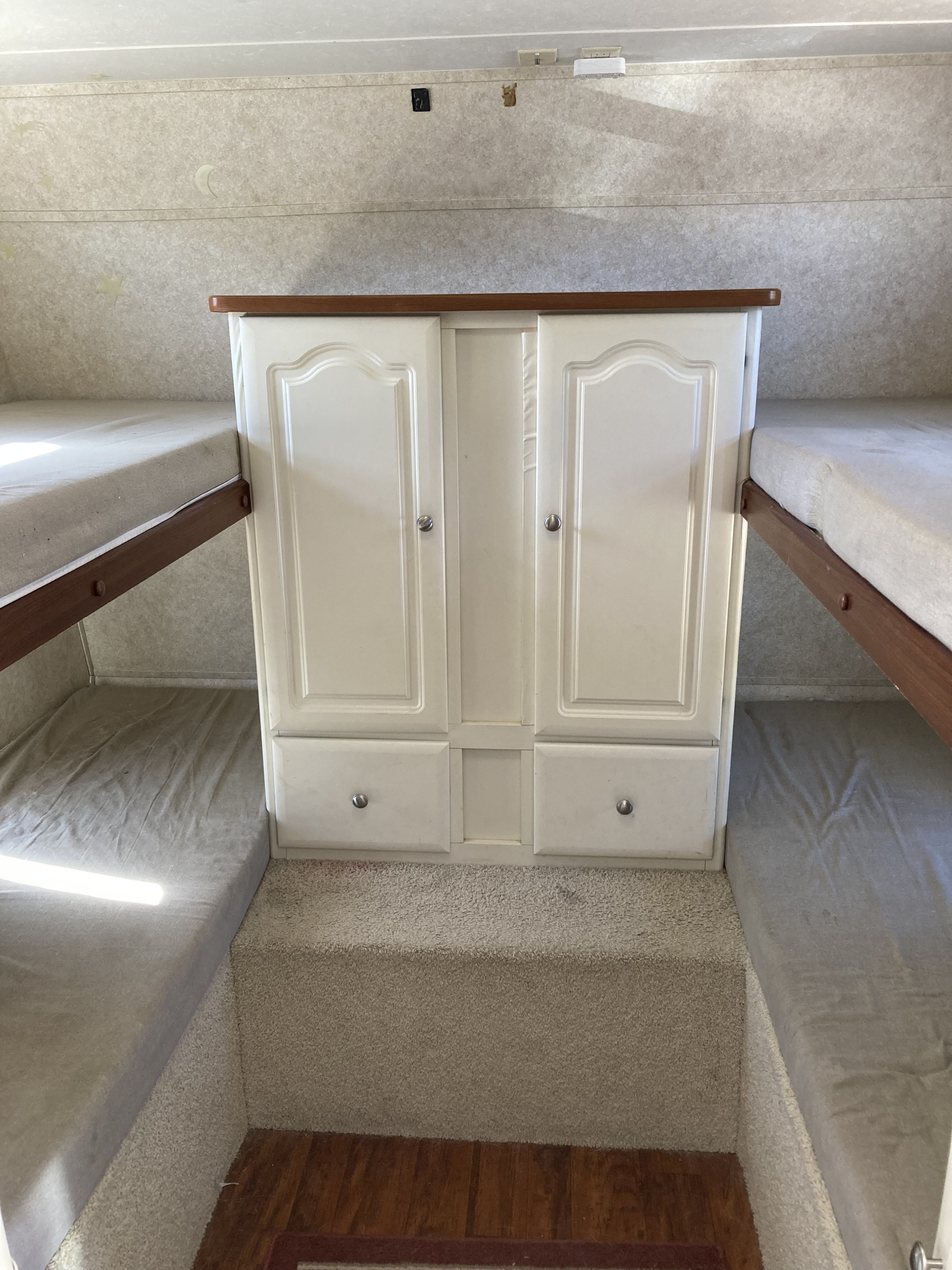 RV rental bunk beds with a central storage cabinet and carpeted floor, offering a cozy, compact sleeping area.. Keystone RV Outback 2005