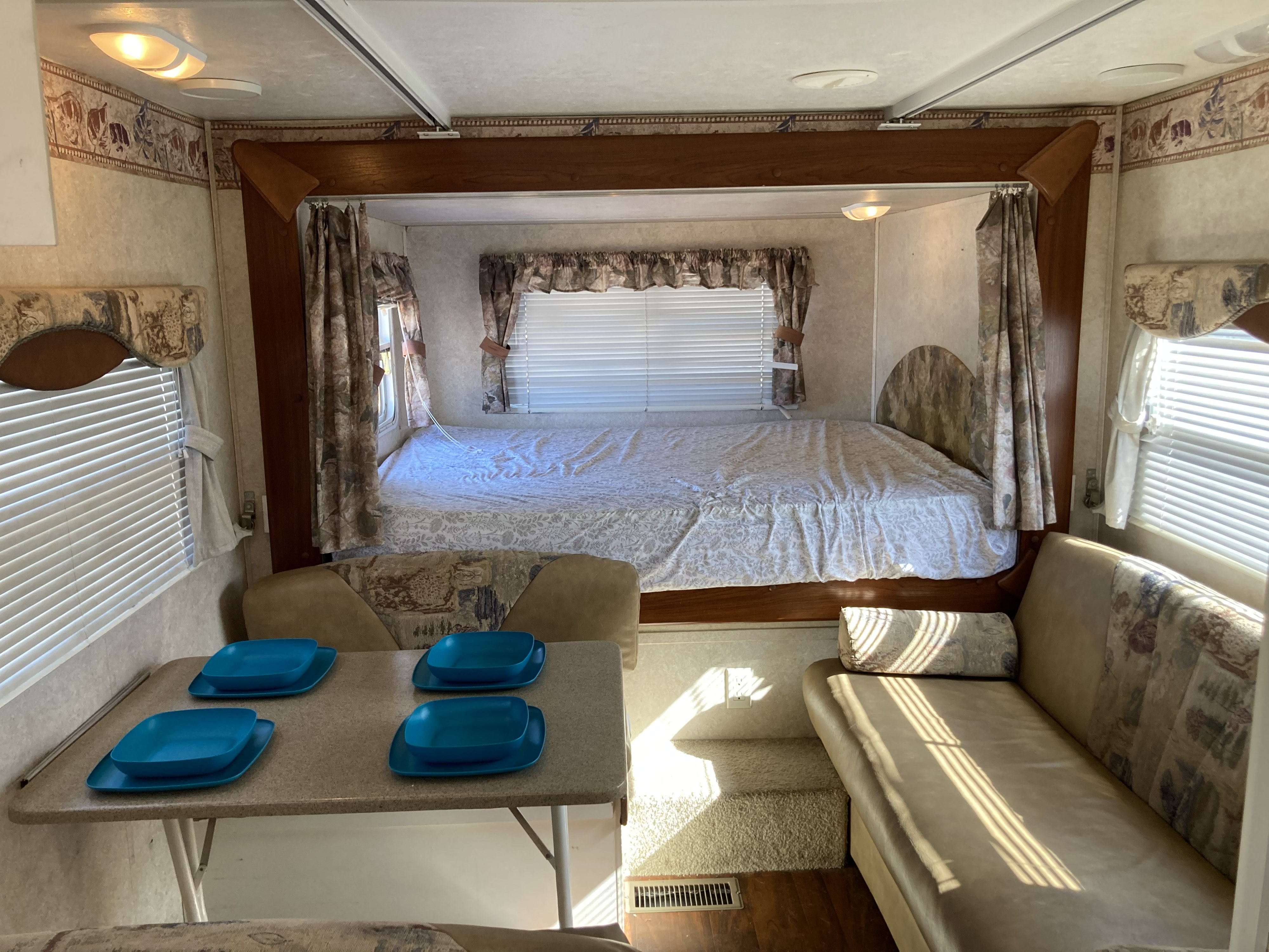 This RV rental interior offers a comfortable stay, with a bed, dining area featuring blue plates, and a cozy couch.. Keystone RV Outback 2005