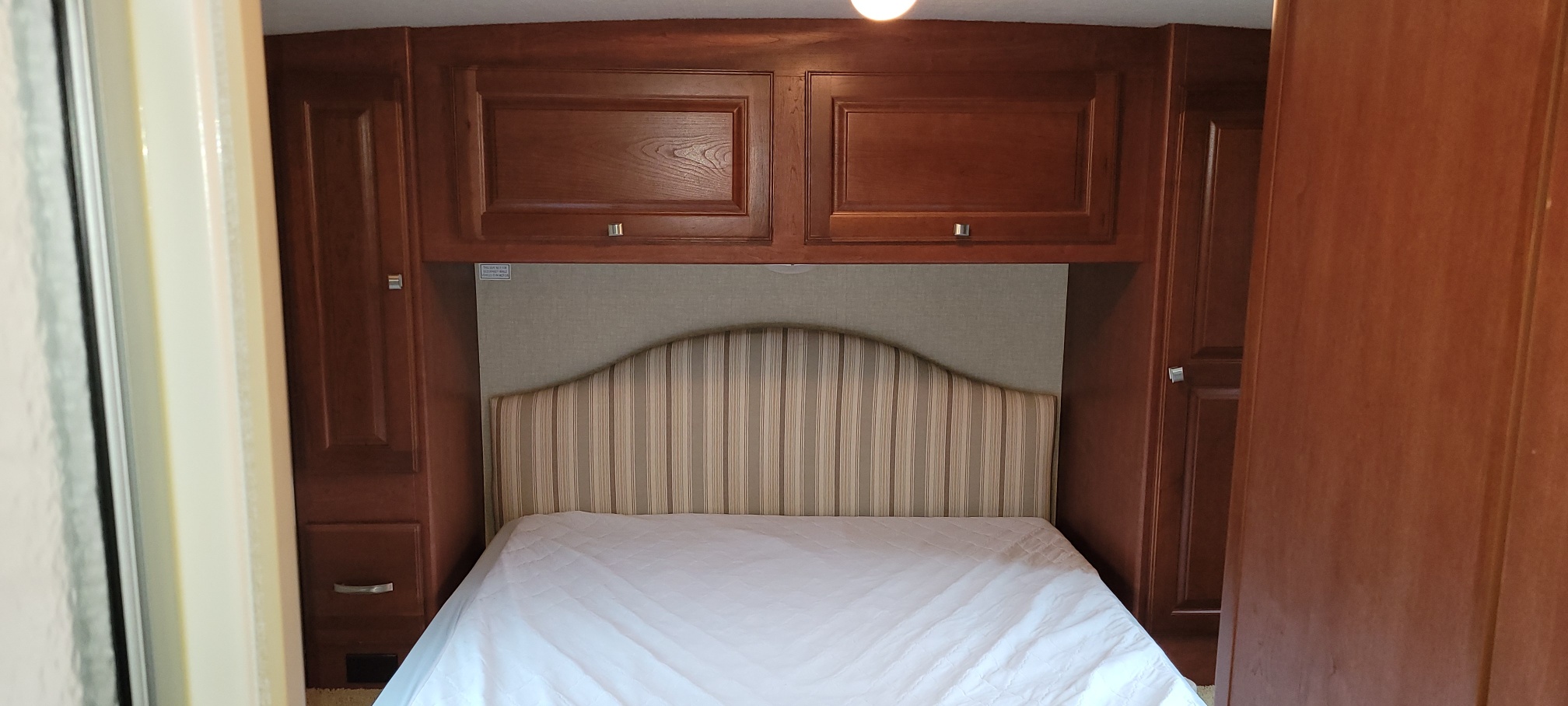 Compact RV rental bedroom featuring a striped headboard, white bed, and built-in wooden cabinets.. Itasca other 2014